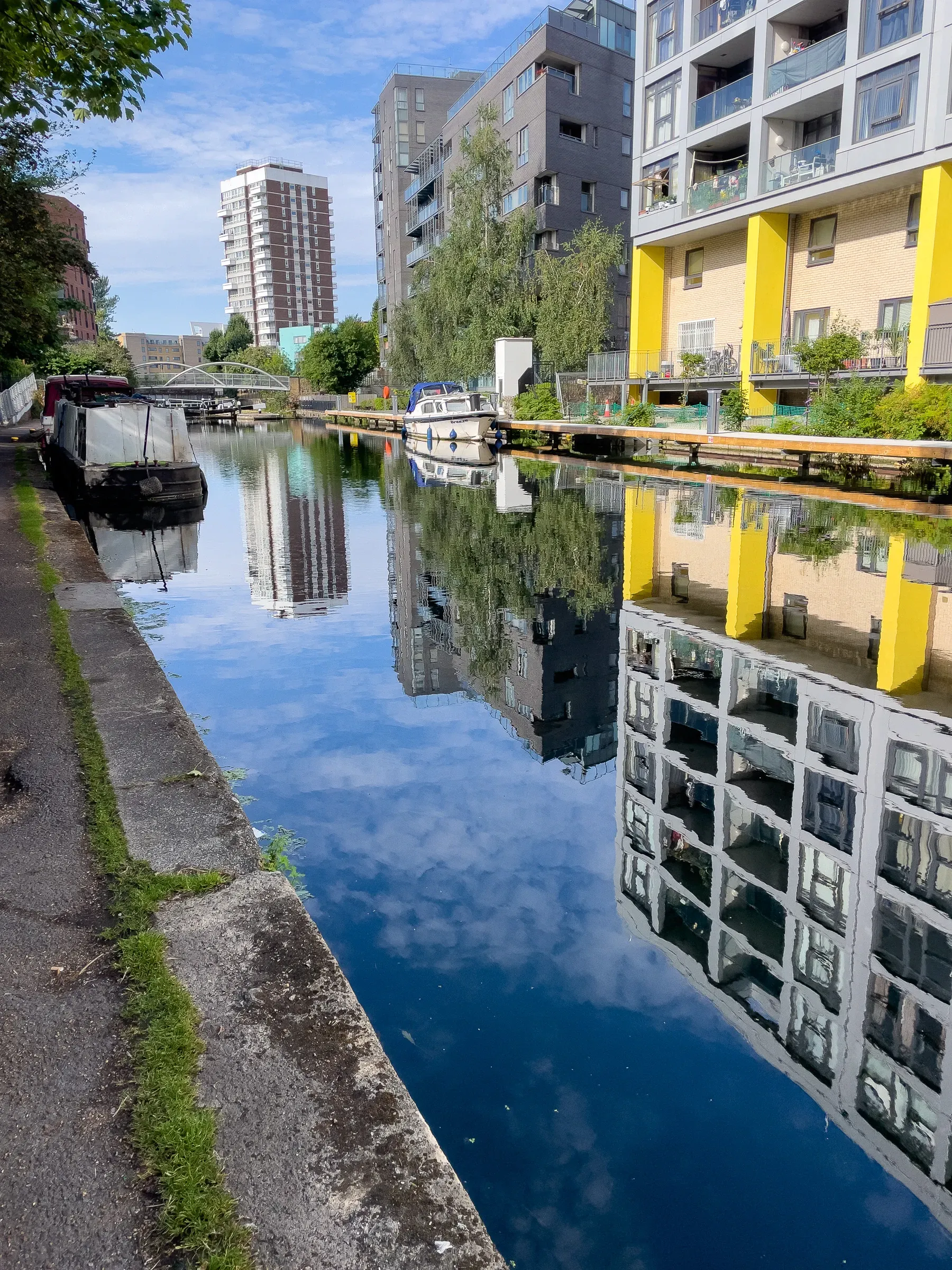 Looking along the Regent's Canal — narrowboats moored left, modern apartments with yellow columns reflected in still water
