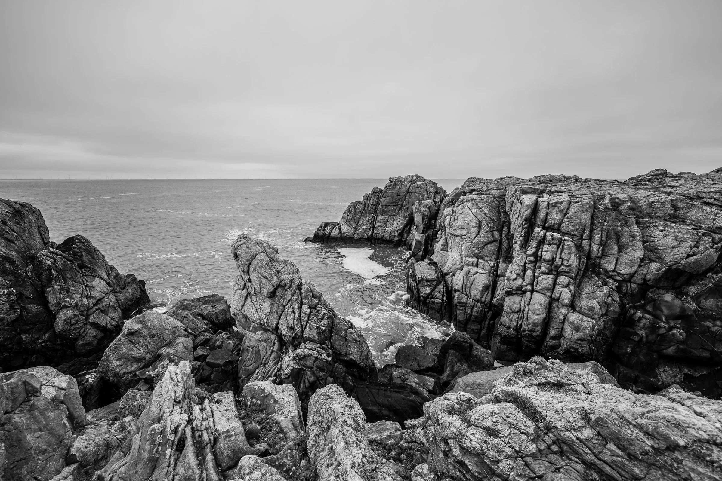 Black and white — jagged granite rock formations on the Atlantic coast, waves breaking below, grey sky