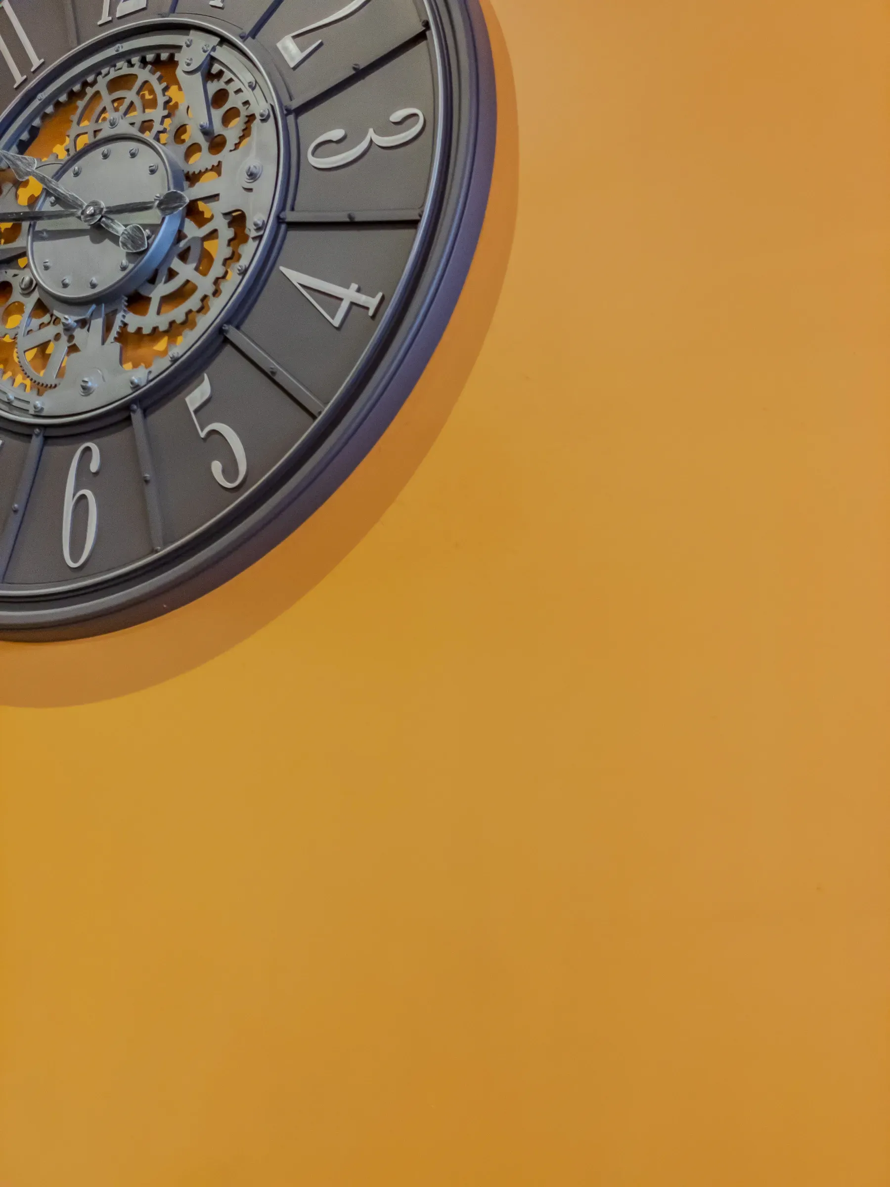 Lower-left quadrant of a skeleton gear clock with exposed mechanism, cropped against a flat orange wall, Toulouse