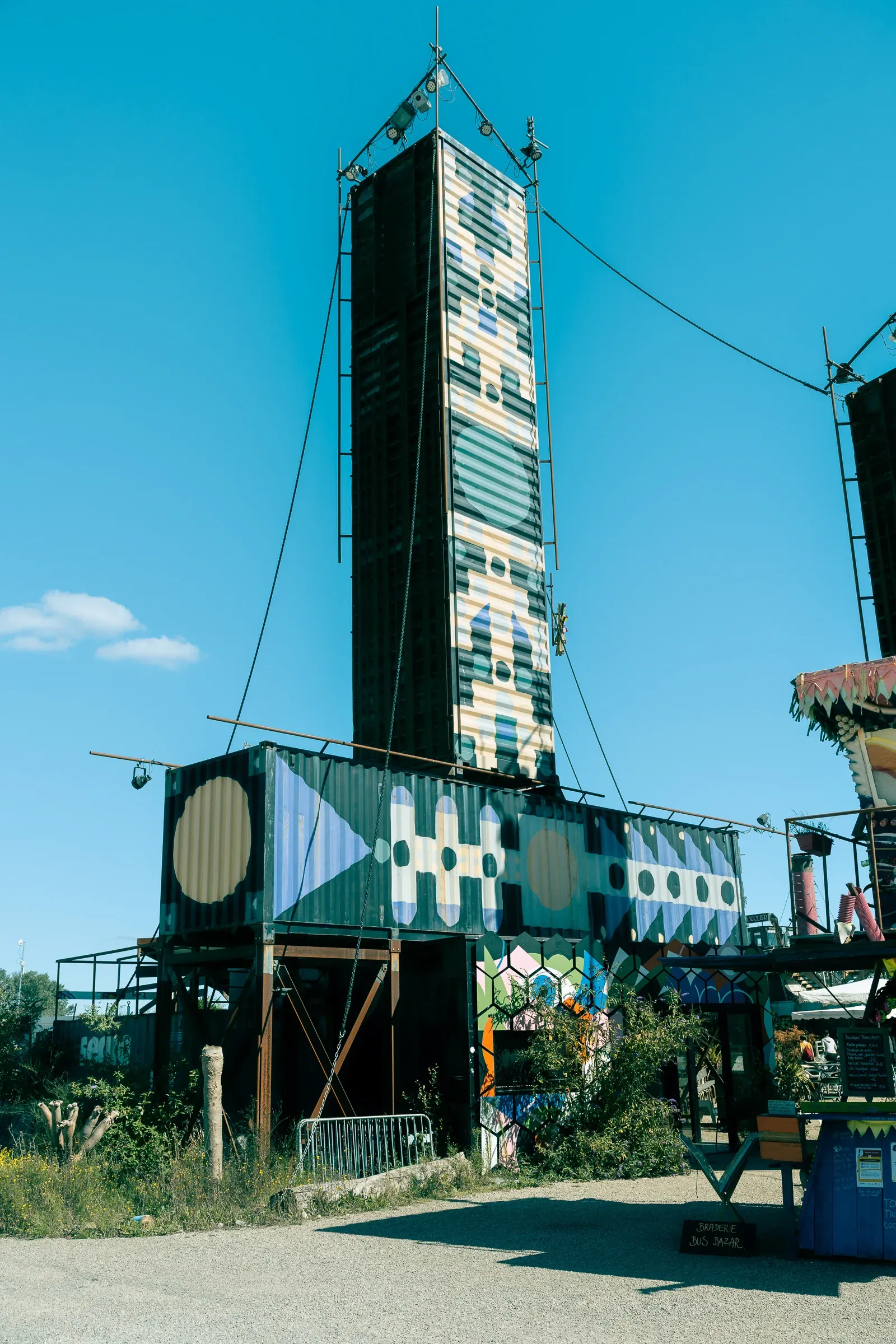 Tall painted shipping container tower with geometric patterns rising against a blue sky, Transfer Autolargue, Nantes