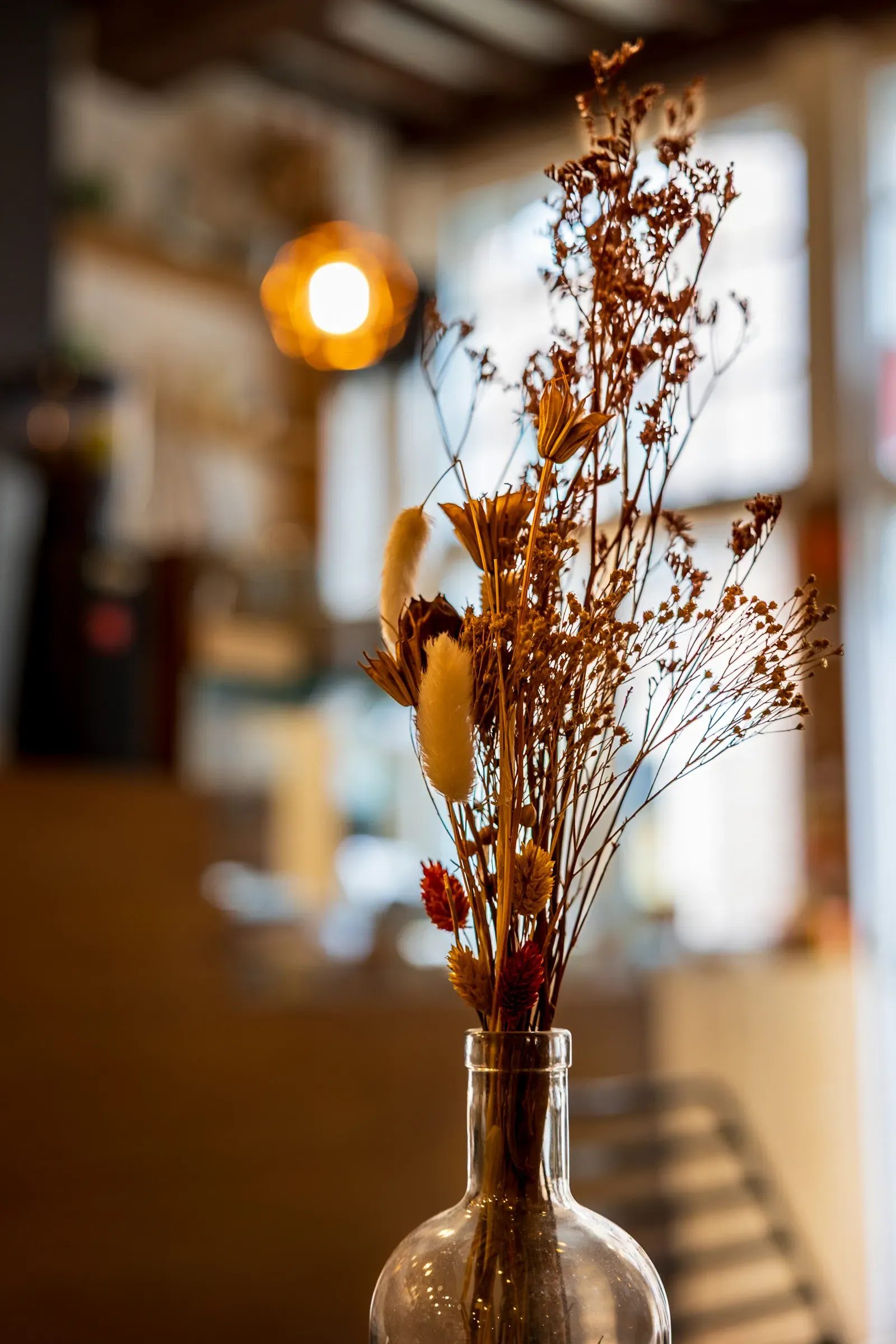 Dried flower bouquet in a glass bottle on a cafe counter, warm light bokeh behind