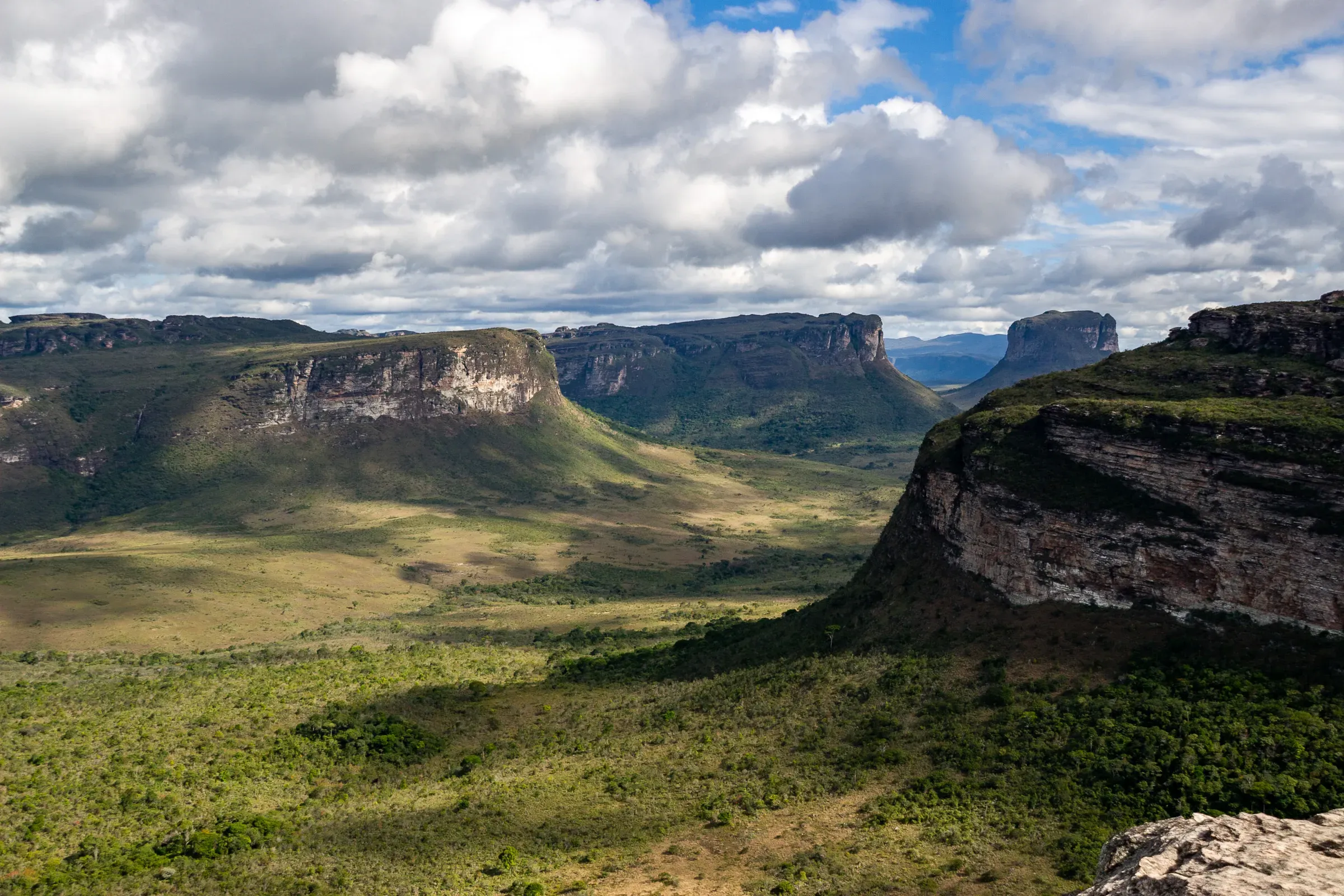 Wide valley between flat-topped sandstone plateaus, Chapada Diamantina — lush green floor, dramatic cloud formations overhead