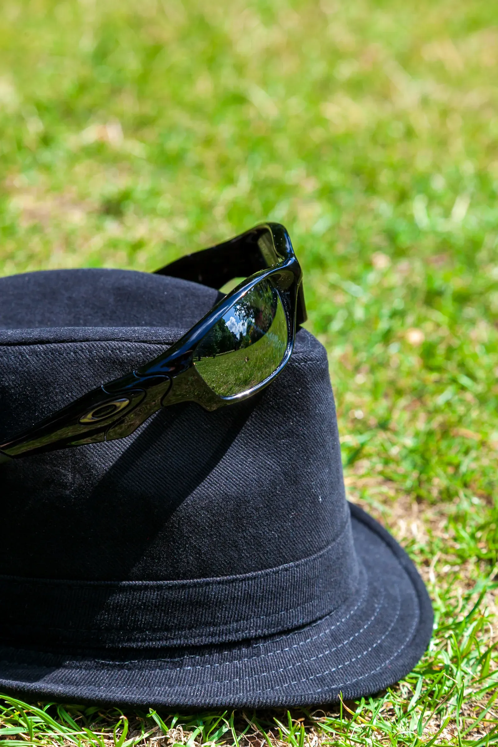 A black felt hat and dark sunglasses resting on short green grass in a London park