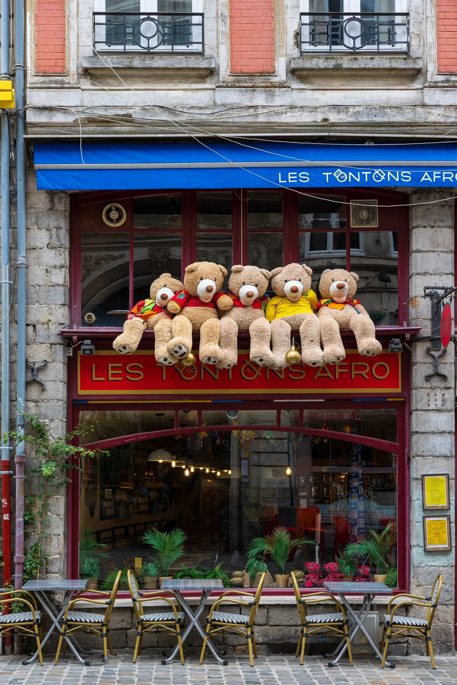 Row of giant dressed teddy bears sitting on the upper storefront ledge of Les Tontons Afro restaurant, Lille