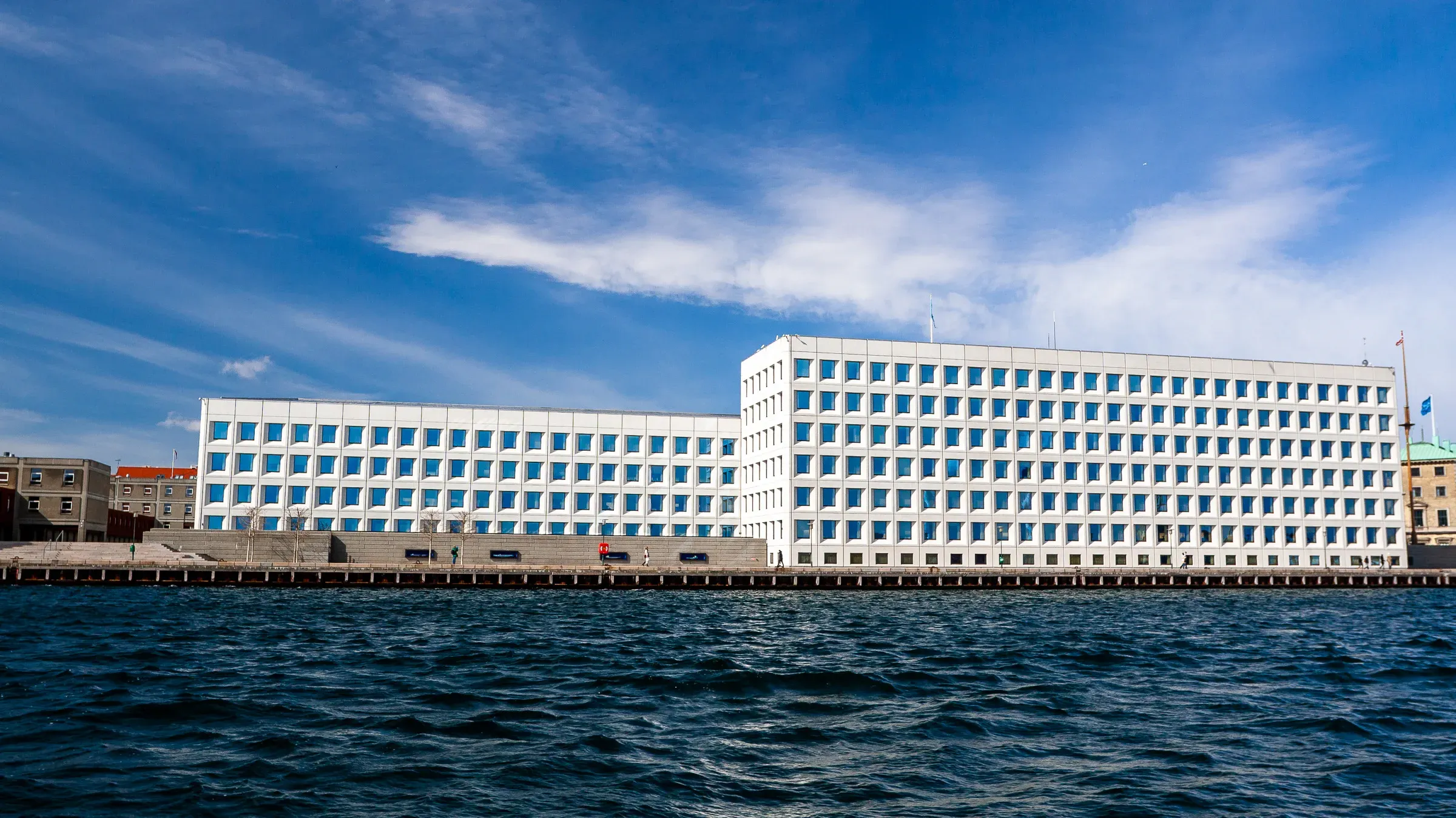 White modernist building seen from across the water under a blue sky