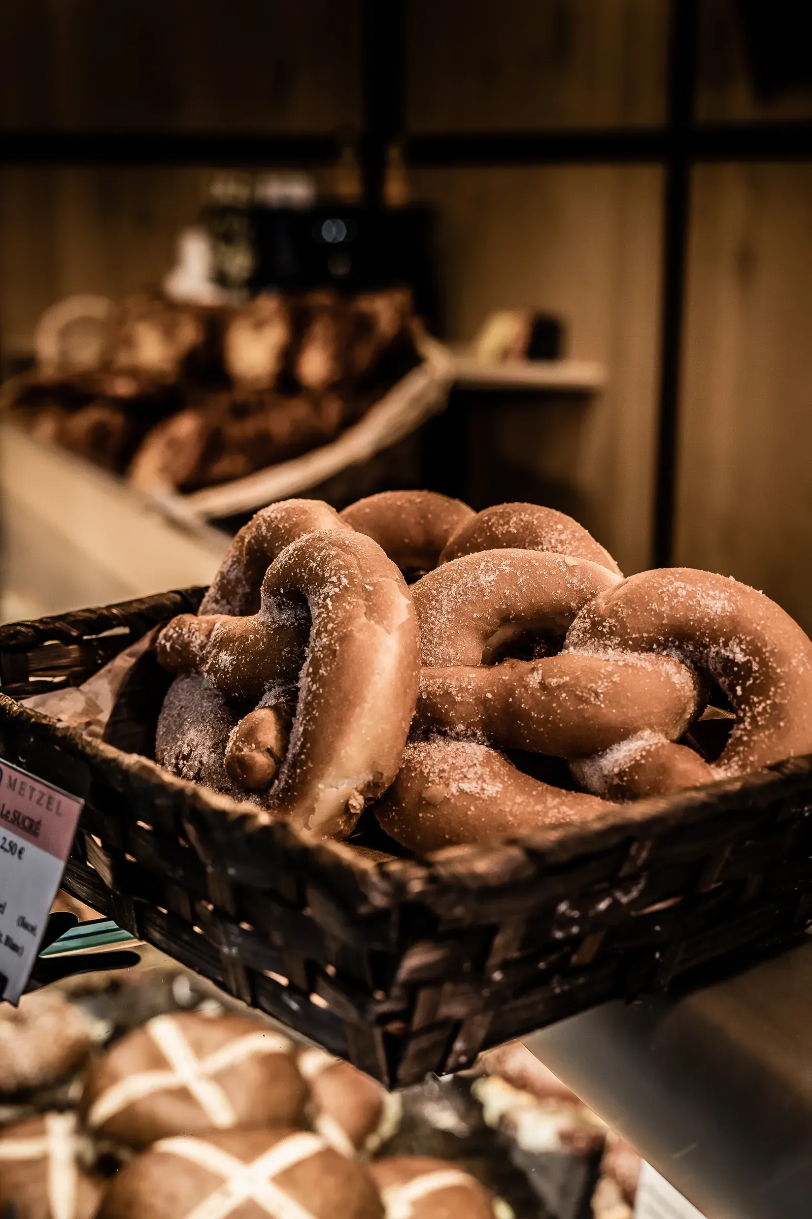Wicker basket of large pretzels in a bakery display, warm dark light, more pastries on shelves behind
