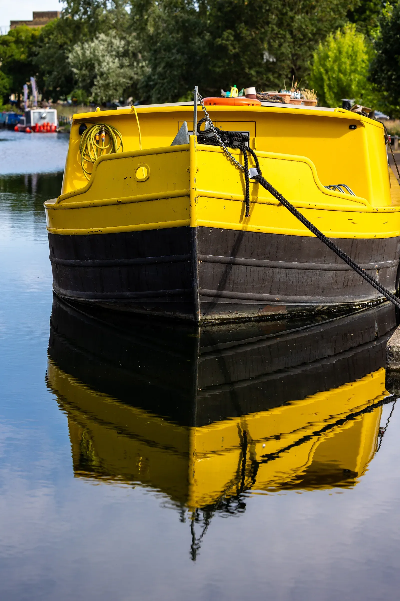 Bow of a bold yellow and black narrowboat reflected sharp in the green canal water