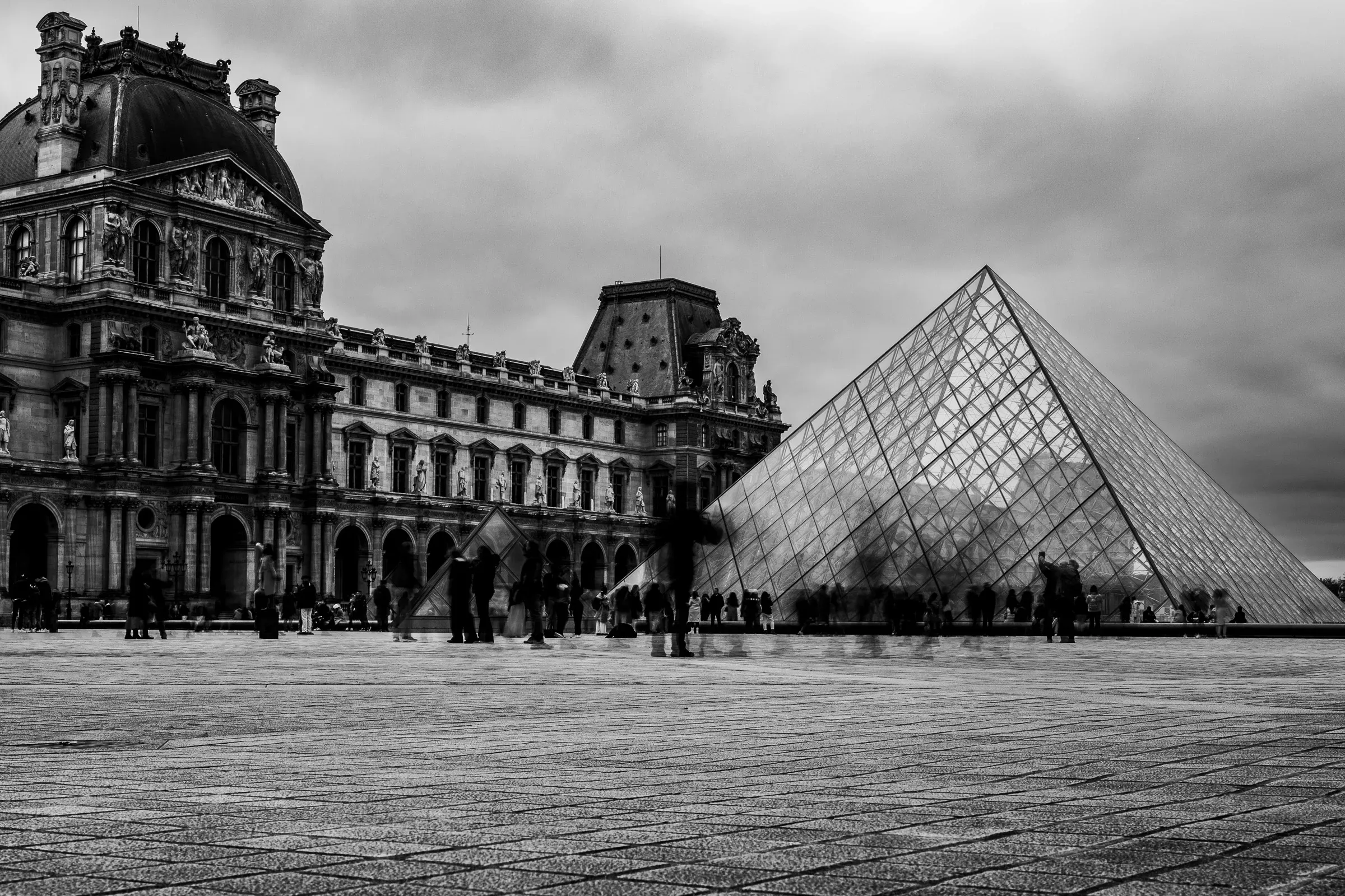 The Louvre pyramid and palace facade, with blurred crowds moving through the courtyard