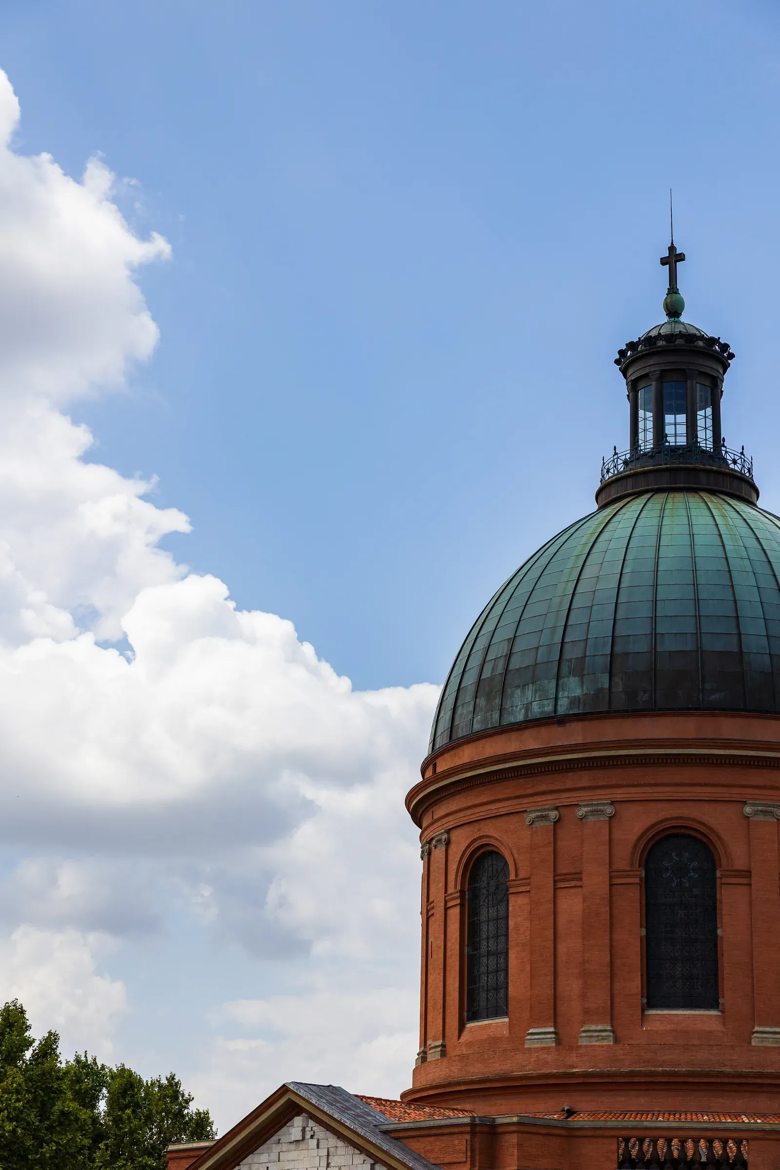 The oxidized copper dome and upper brick drum of the Hôtel-Dieu Saint-Jacques, cross at the top, against a blue sky with scattered clouds, Toulouse