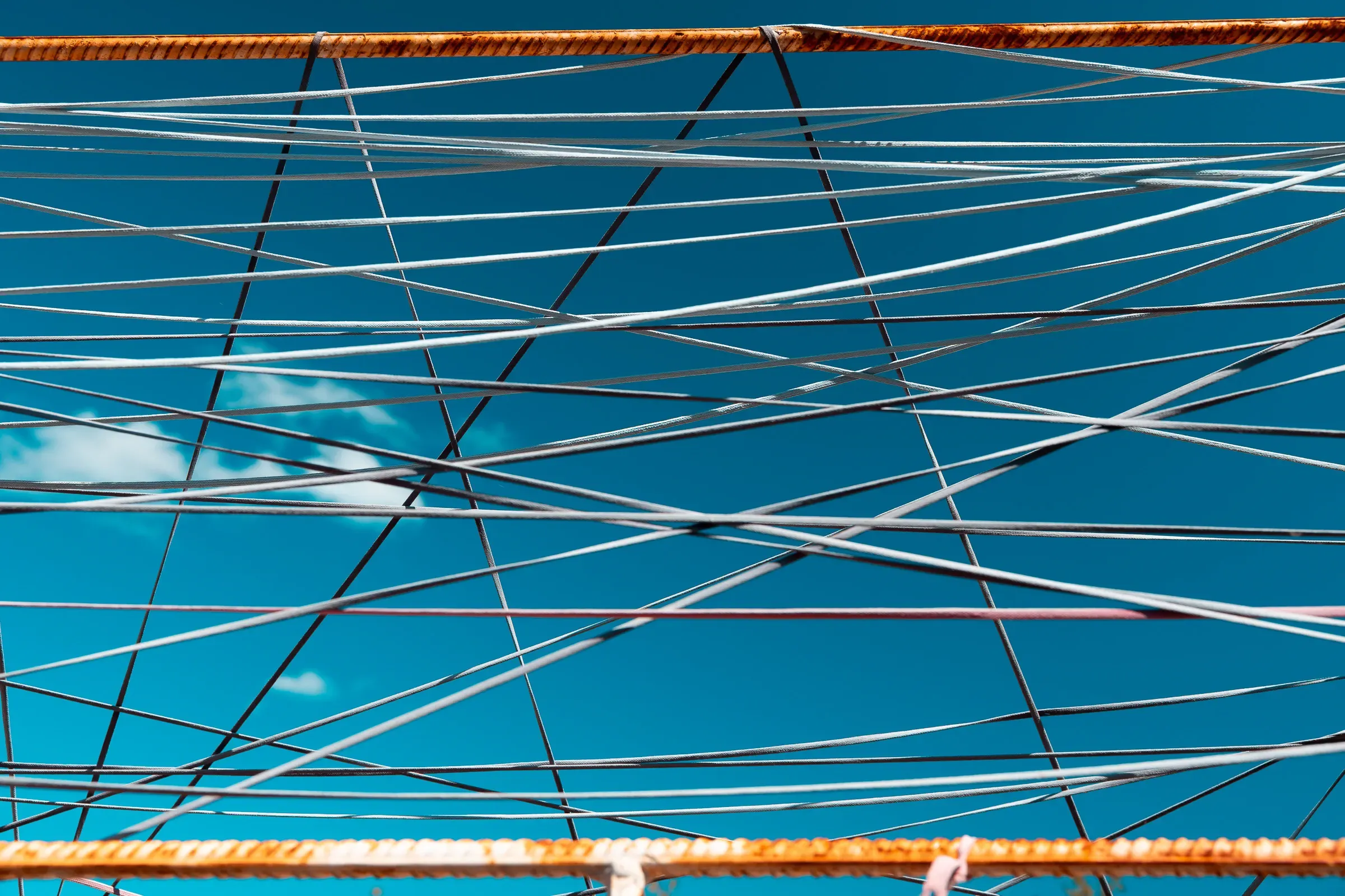 Abstract pattern of crossed metal cables and wires against a bright blue sky