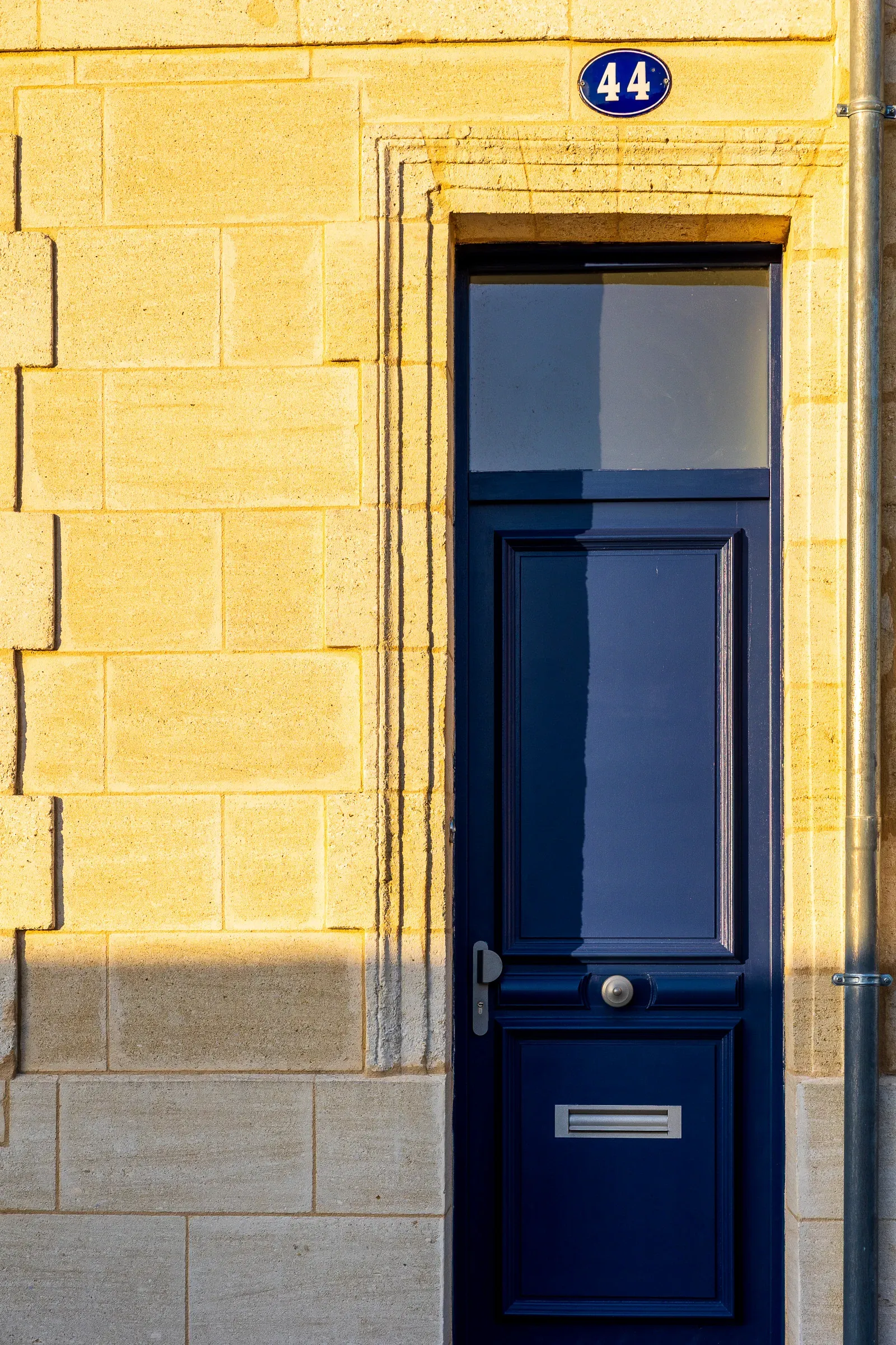 Navy blue door numbered 44 set into a golden limestone wall bathed in warm afternoon light, Bordeaux