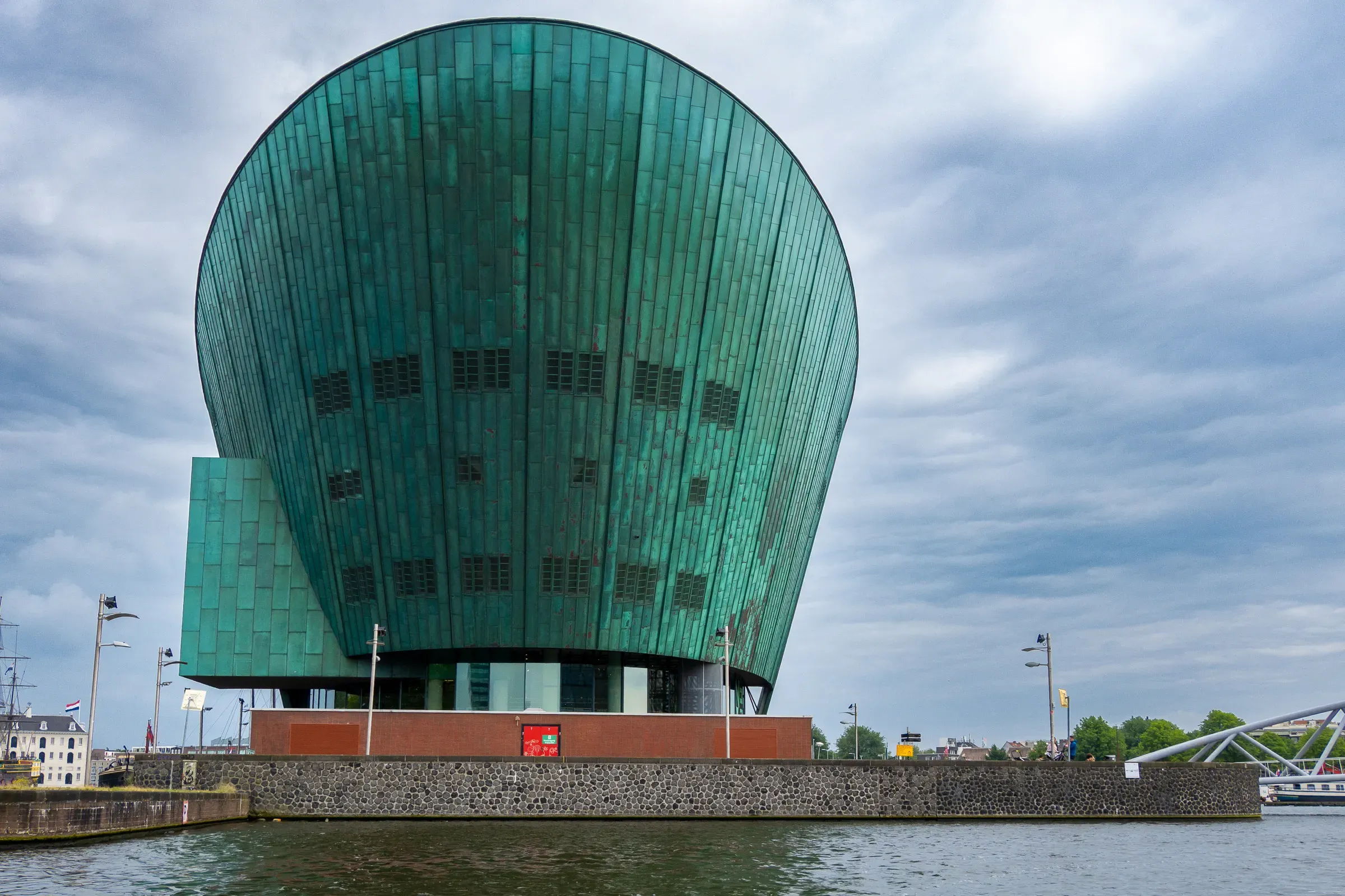 The green copper hull of the NEMO Science Museum seen from the water under a heavy overcast sky