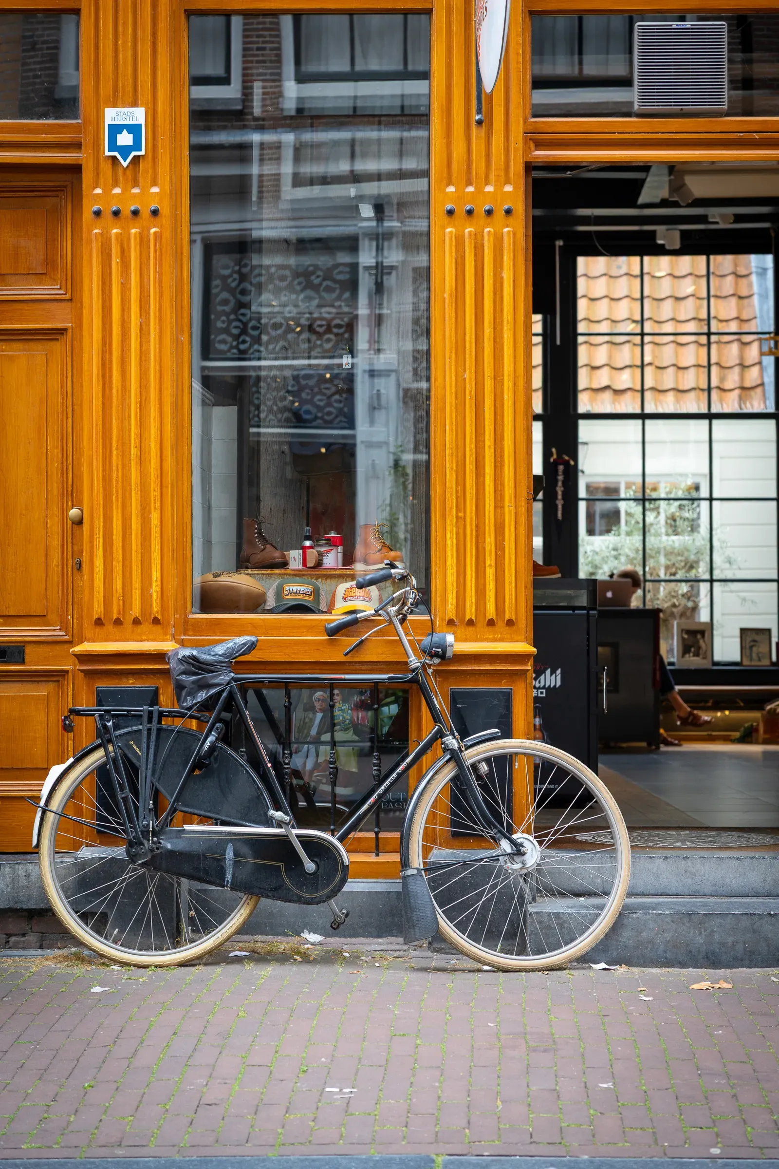 A classic black Dutch city bike leaning against a warm amber wooden shopfront, Amsterdam