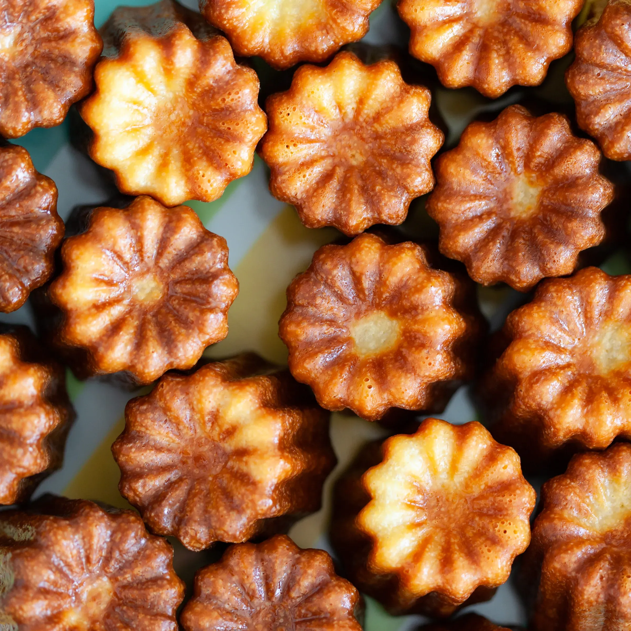 Overhead close-up of cannelés bordelais — dark golden ridged cylinders packed tightly together, caramelised crust catching the light