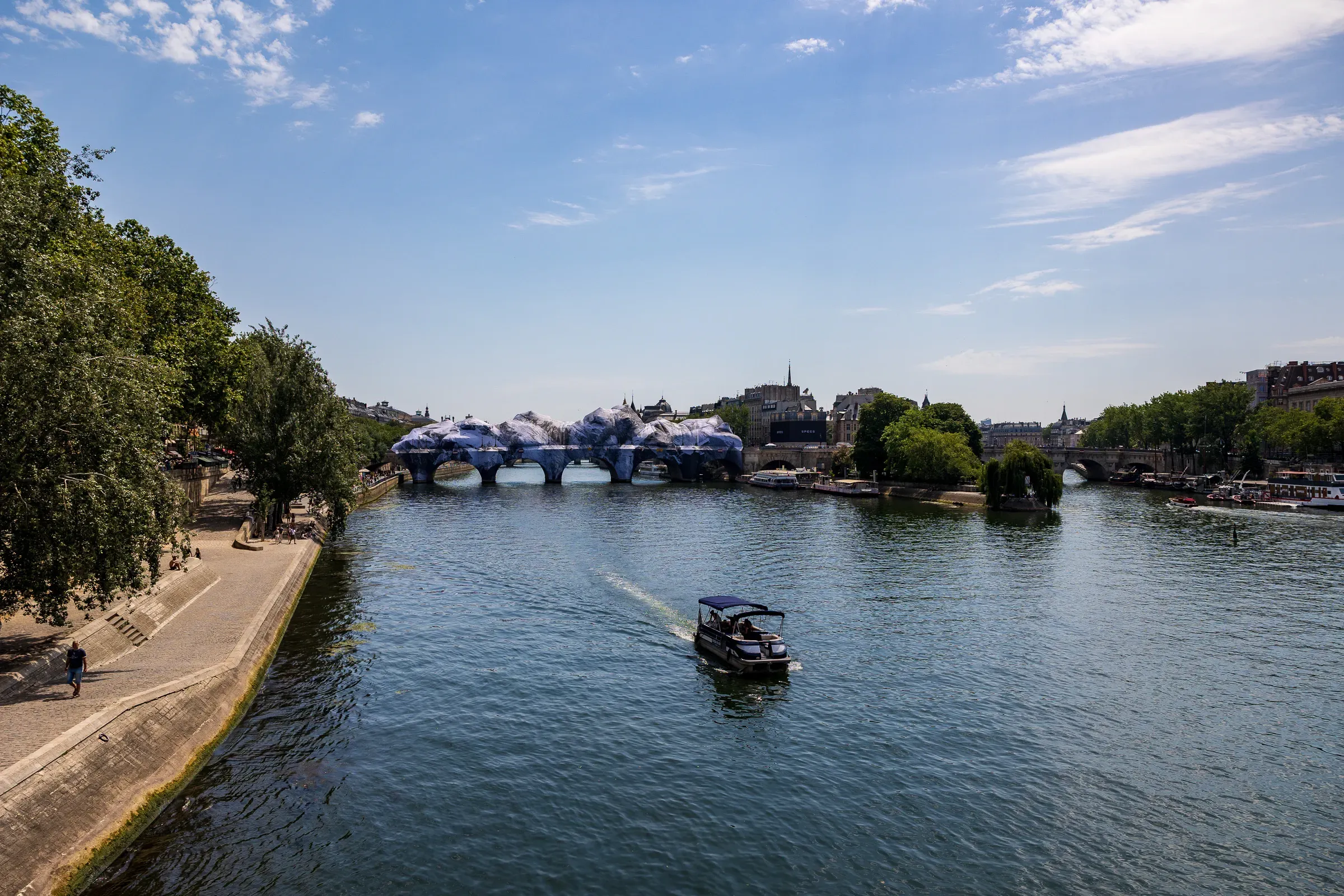 A Seine tour boat passing close in front of the wrapped Pont Neuf, its cave-like trompe-l'œil panels catching the light, Paris