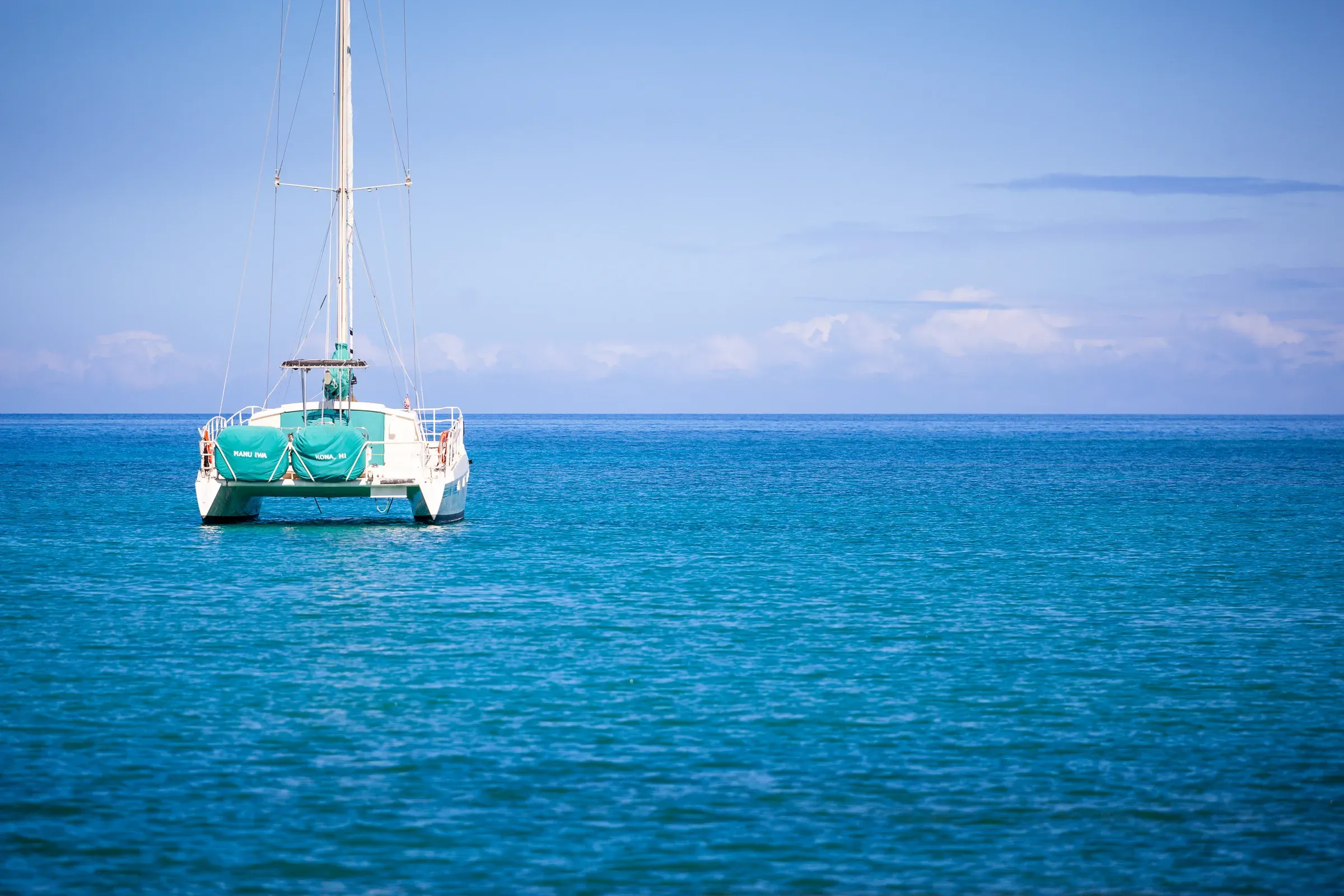 White catamaran anchored on flat turquoise water, Hawaii — clear blue sky, horizon line sharp and unbroken