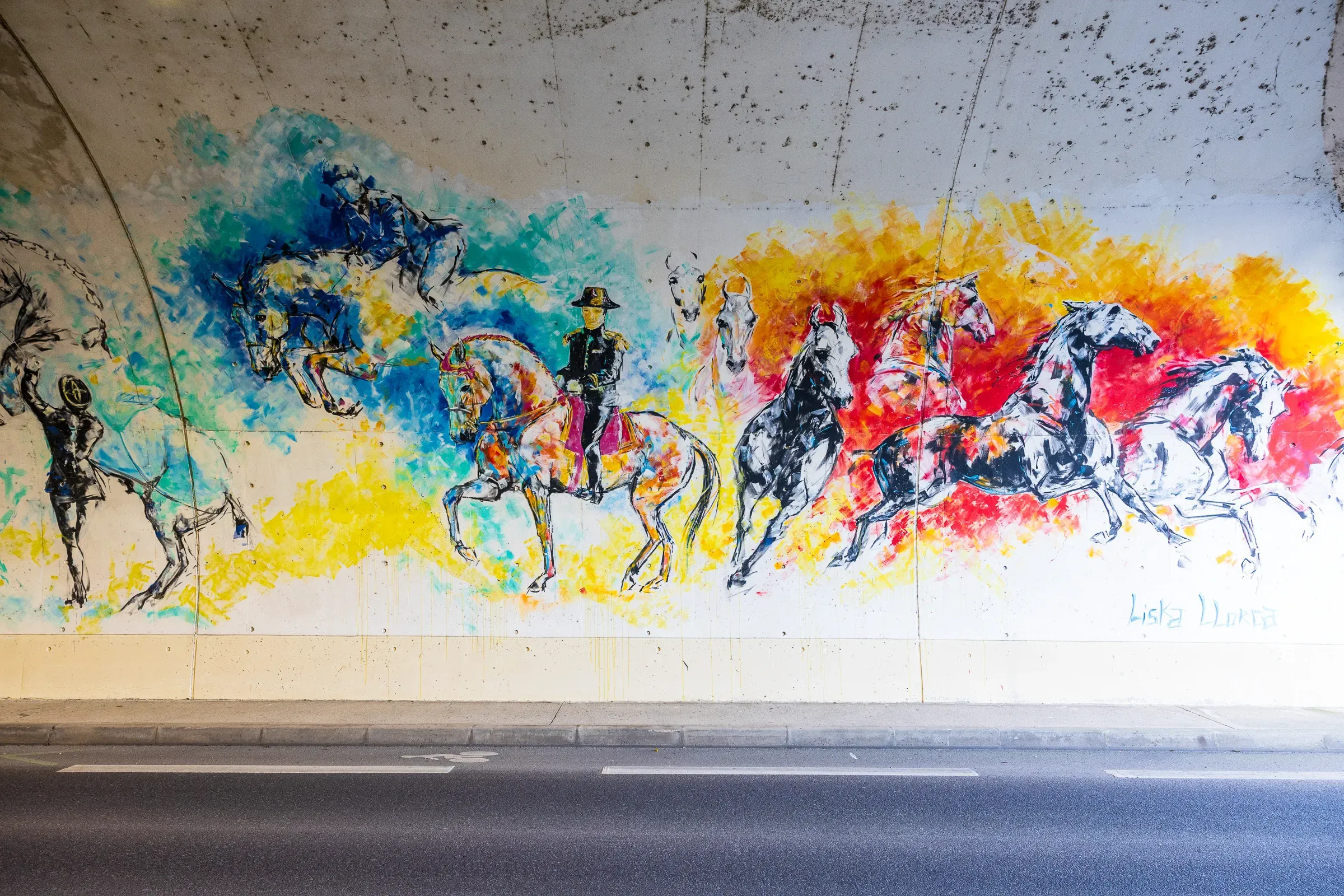 Tunnel underpass mural of horses and an equestrian rider in bold blue, yellow, and red across a concrete wall, Saumur