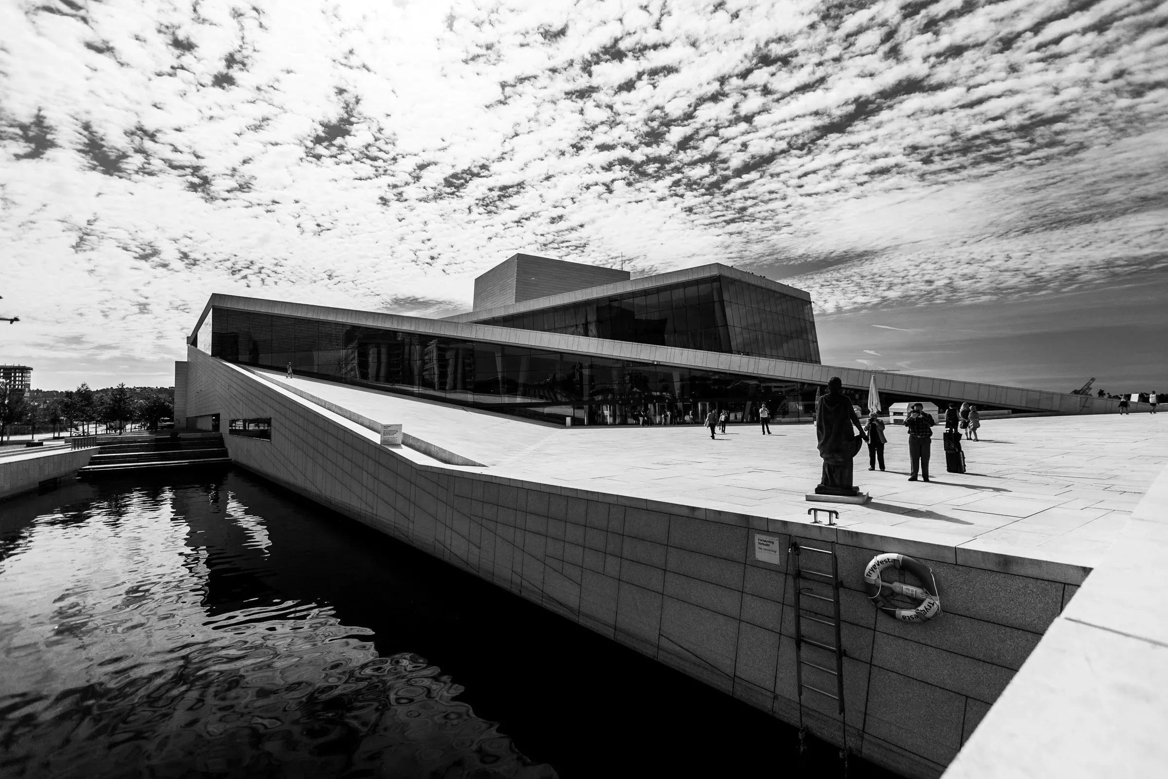 Oslo Opera House seen from the waterfront, its sloping white marble roof meeting the quay, visitors on the terrace, mackerel clouds overhead