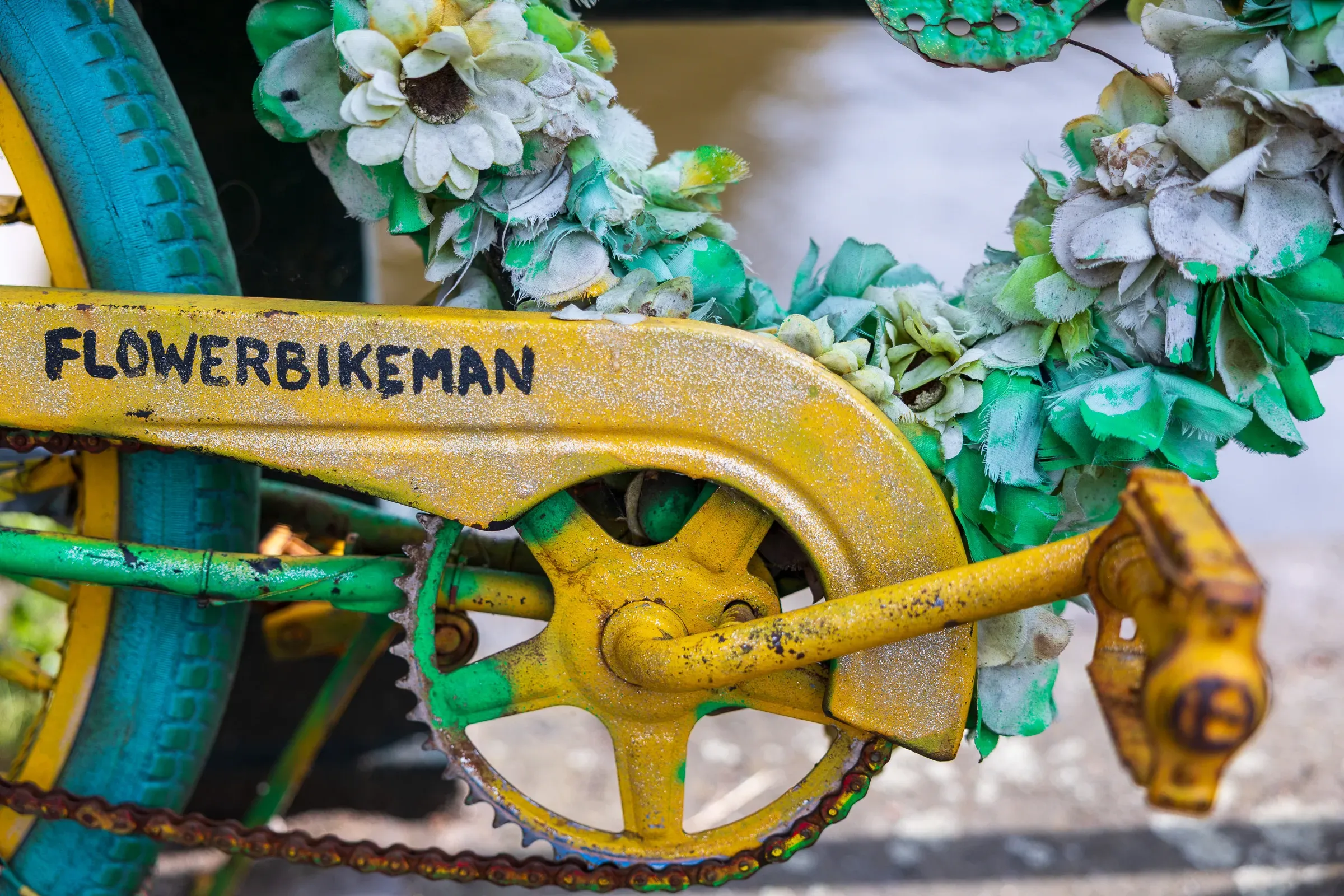 Close-up of a yellow chainring stamped FLOWERBIKEMAN, surrounded by green and yellow floral decorations