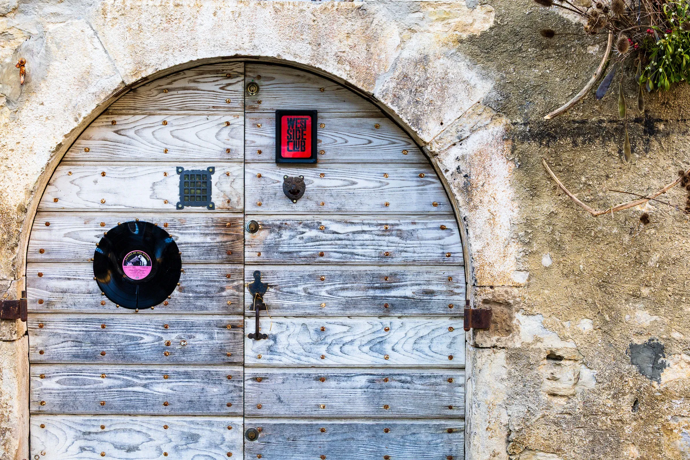 Arched wooden studded door with a vinyl record and a red sticker mounted on it, set in a stone arch, Jura village
