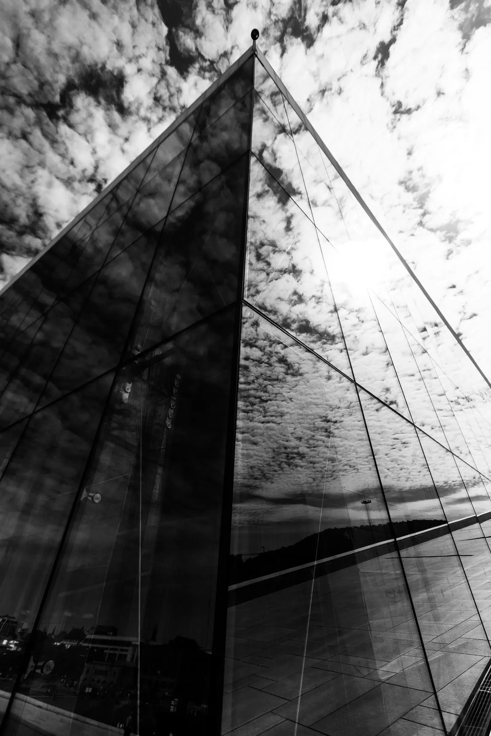 Glass curtain wall of a modern building shot from below at a steep angle, scattered clouds reflected and doubled in the dark panes