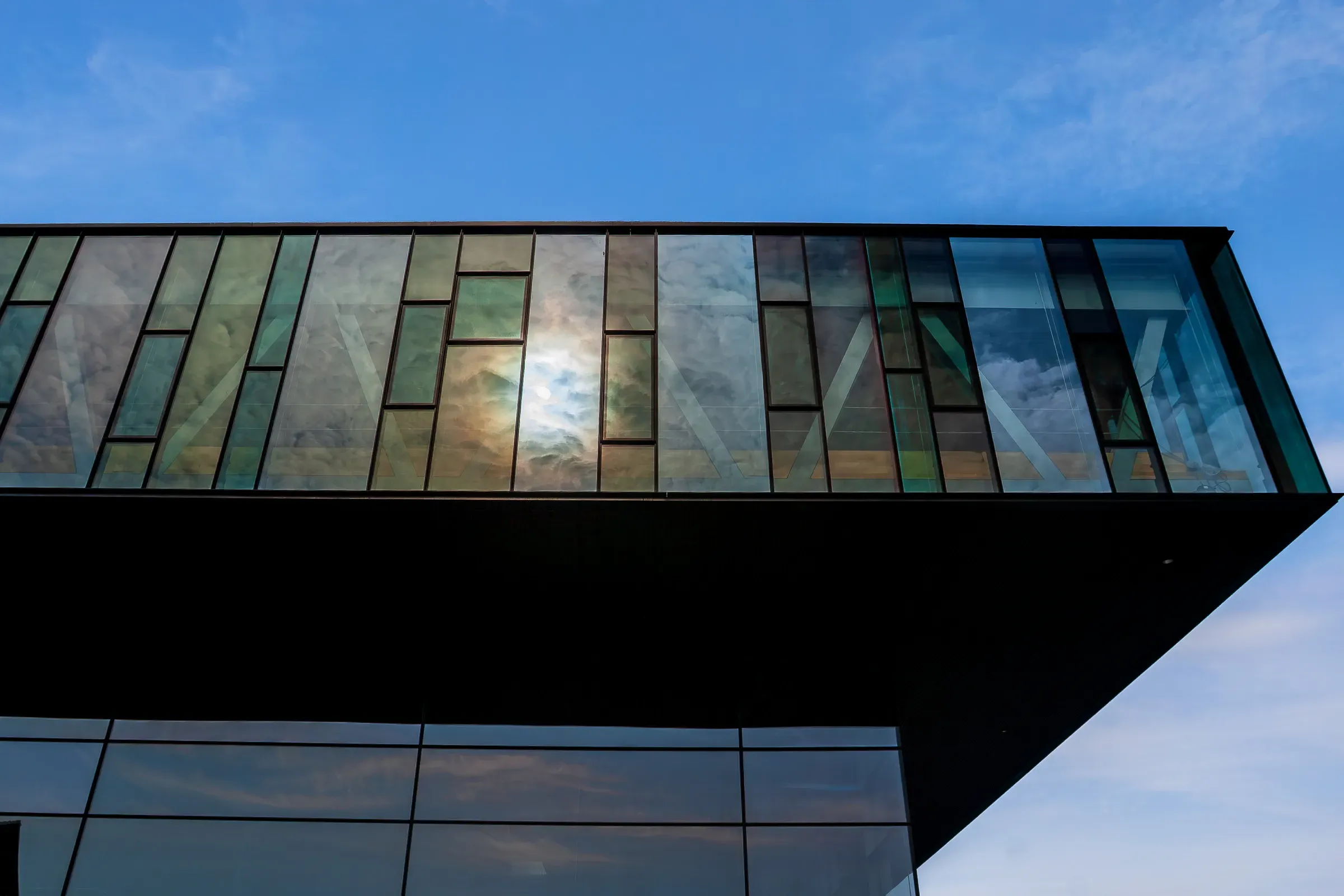 Glass facade of a modern building reflecting clouds and sky, seen from below