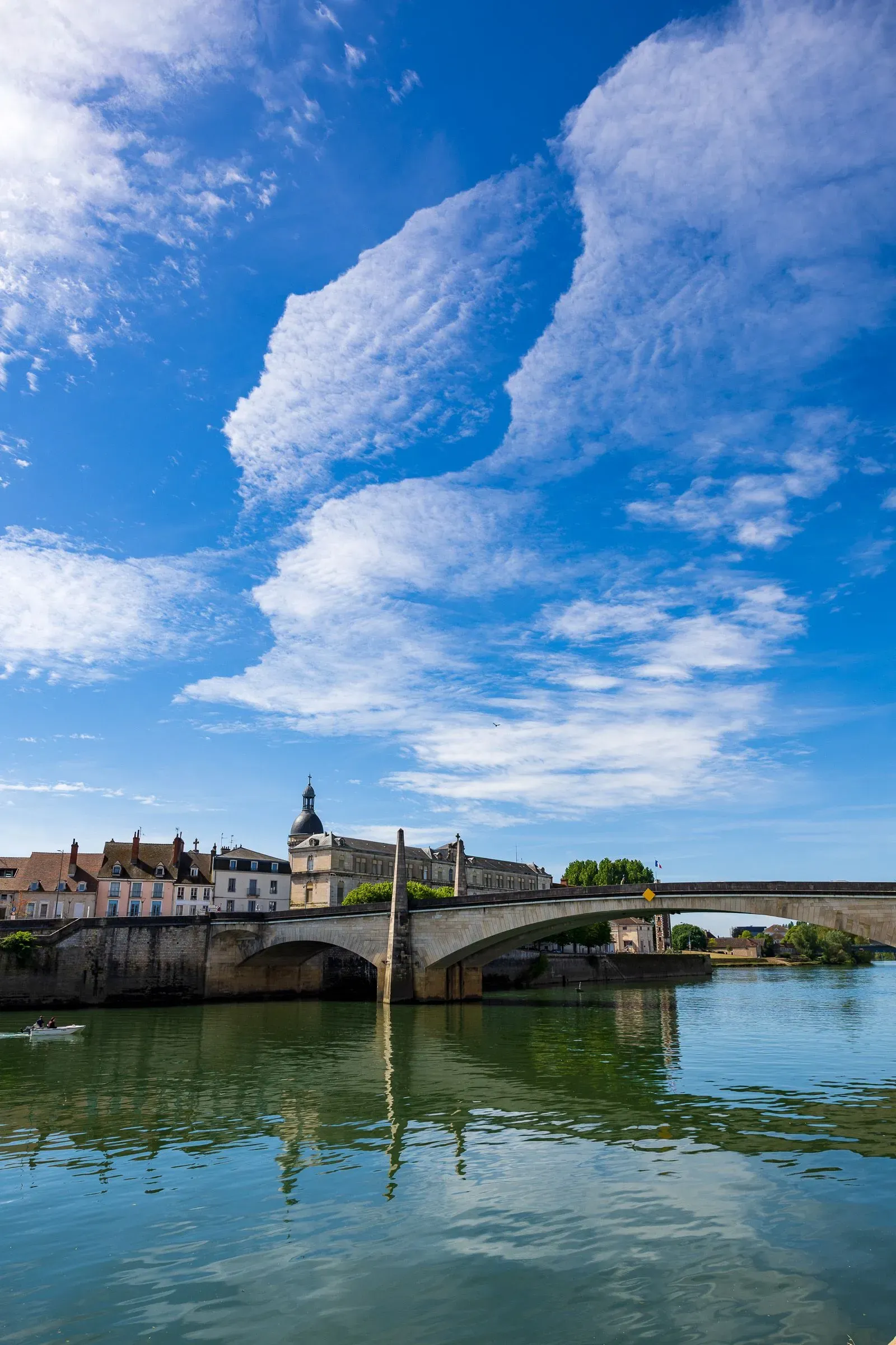 Vertical view of the stone arch bridge over the Saône under a dramatic sky, domed building and bell tower behind, Chalon-sur-Saône