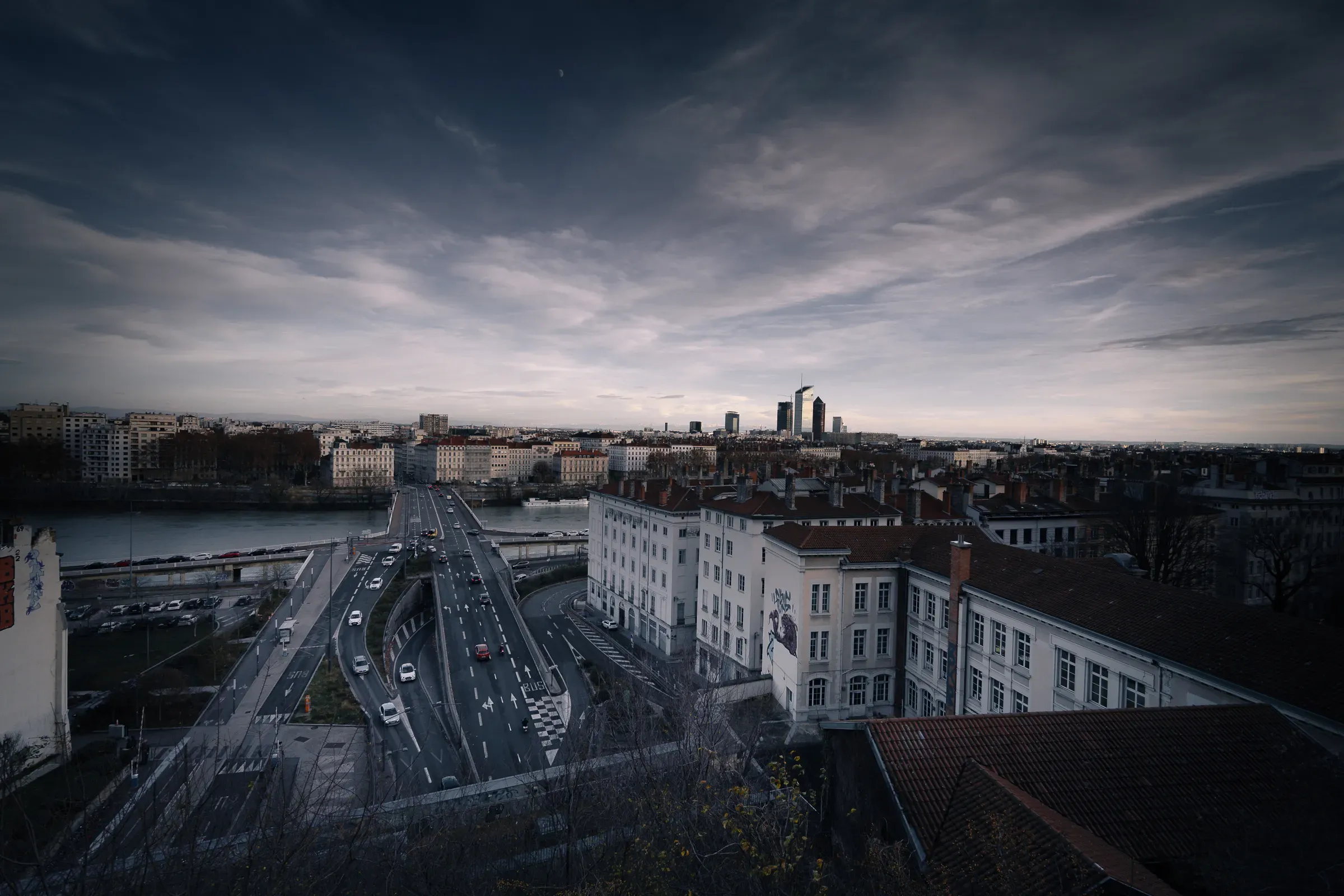 Aerial view of Lyon at dusk with rooftops, highways and the Part-Dieu tower in the distance