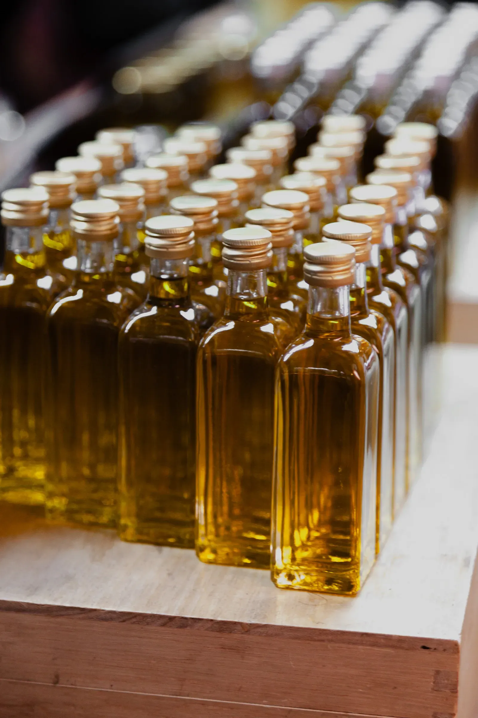 Rows of small square glass bottles filled with golden olive oil, lined up on a wooden display board