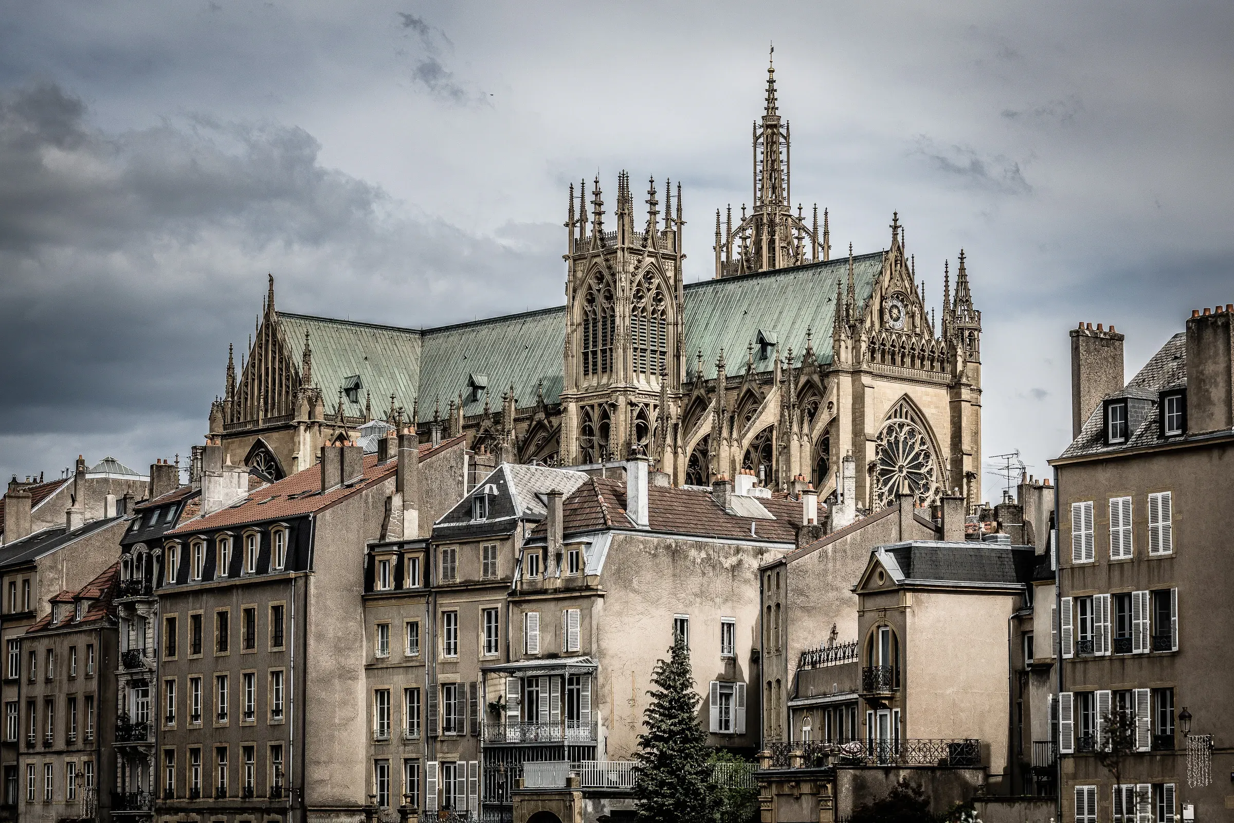 Metz Cathedral rising above the surrounding stone buildings under a dramatic storm sky, green copper roof