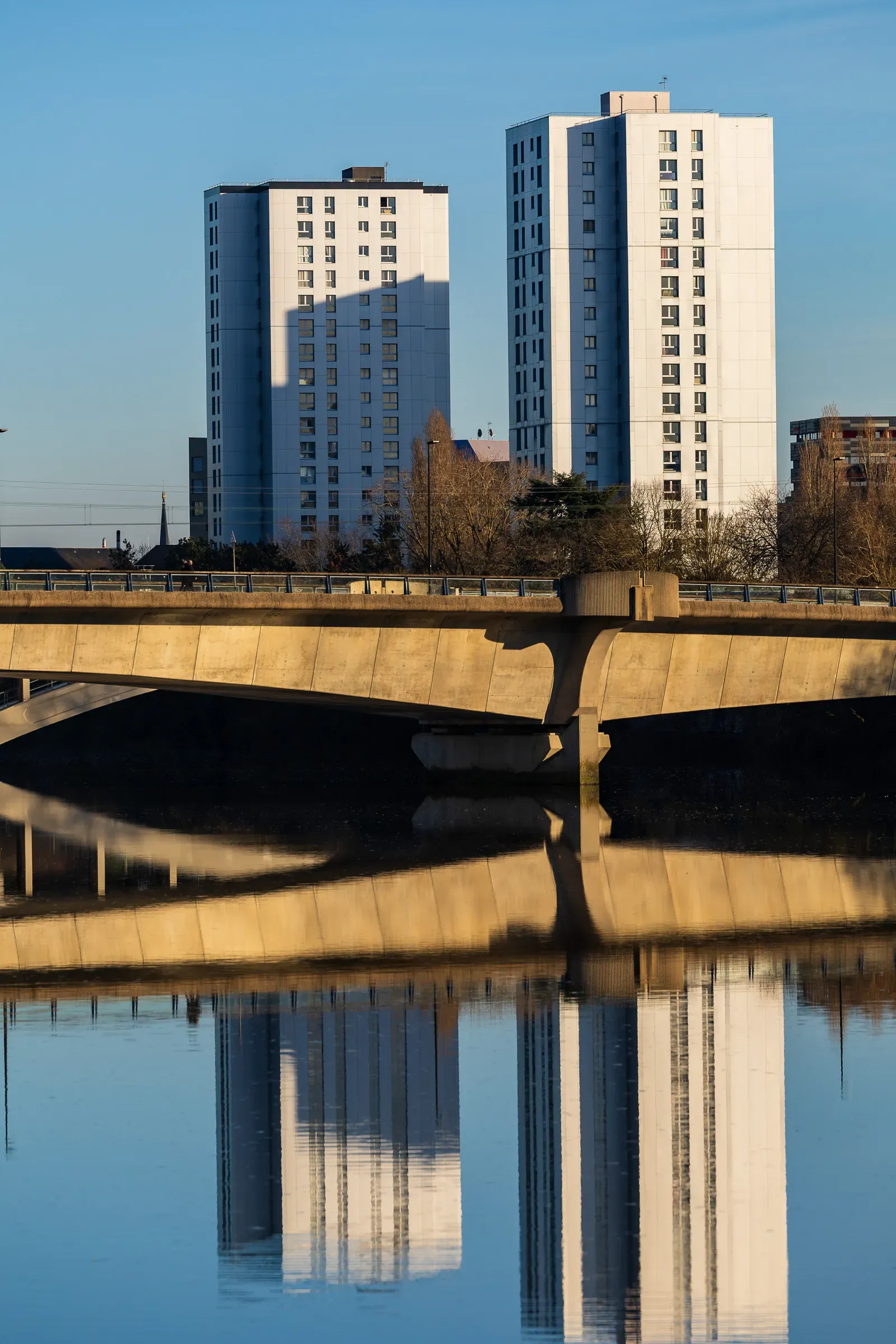 Two white tower blocks and a concrete bridge arch reflected in the still Loire under clear winter light