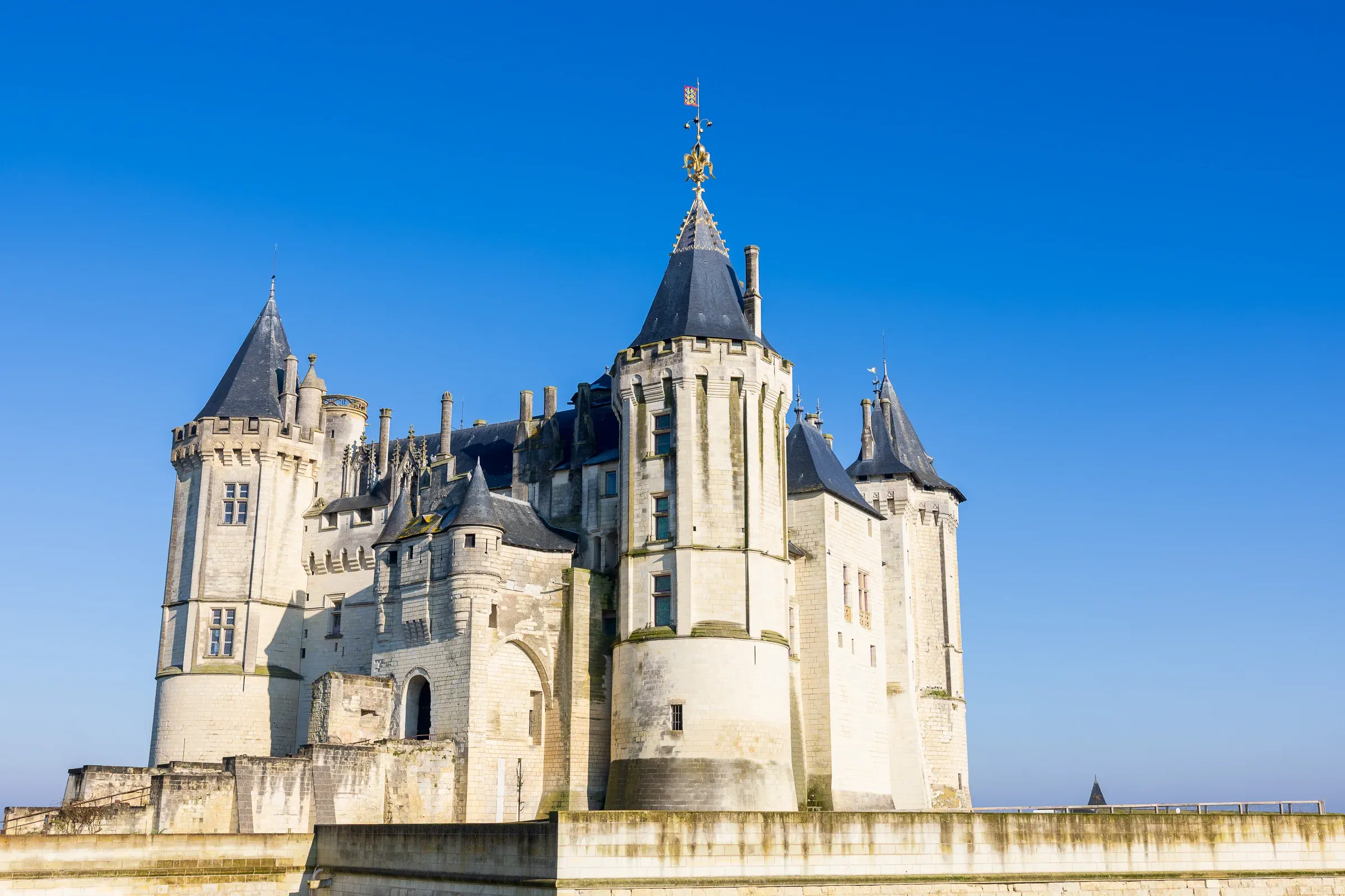 Château de Saumur in winter daylight, white tufa stone towers and slate roofs under a sharp blue sky, Saumur