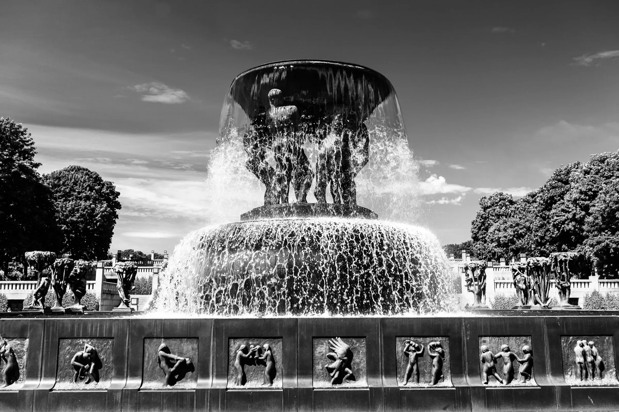 Vigeland Fountain in Frogner Park, Oslo, bronze human figures supporting the great basin as water cascades down in sheets, summer trees behind