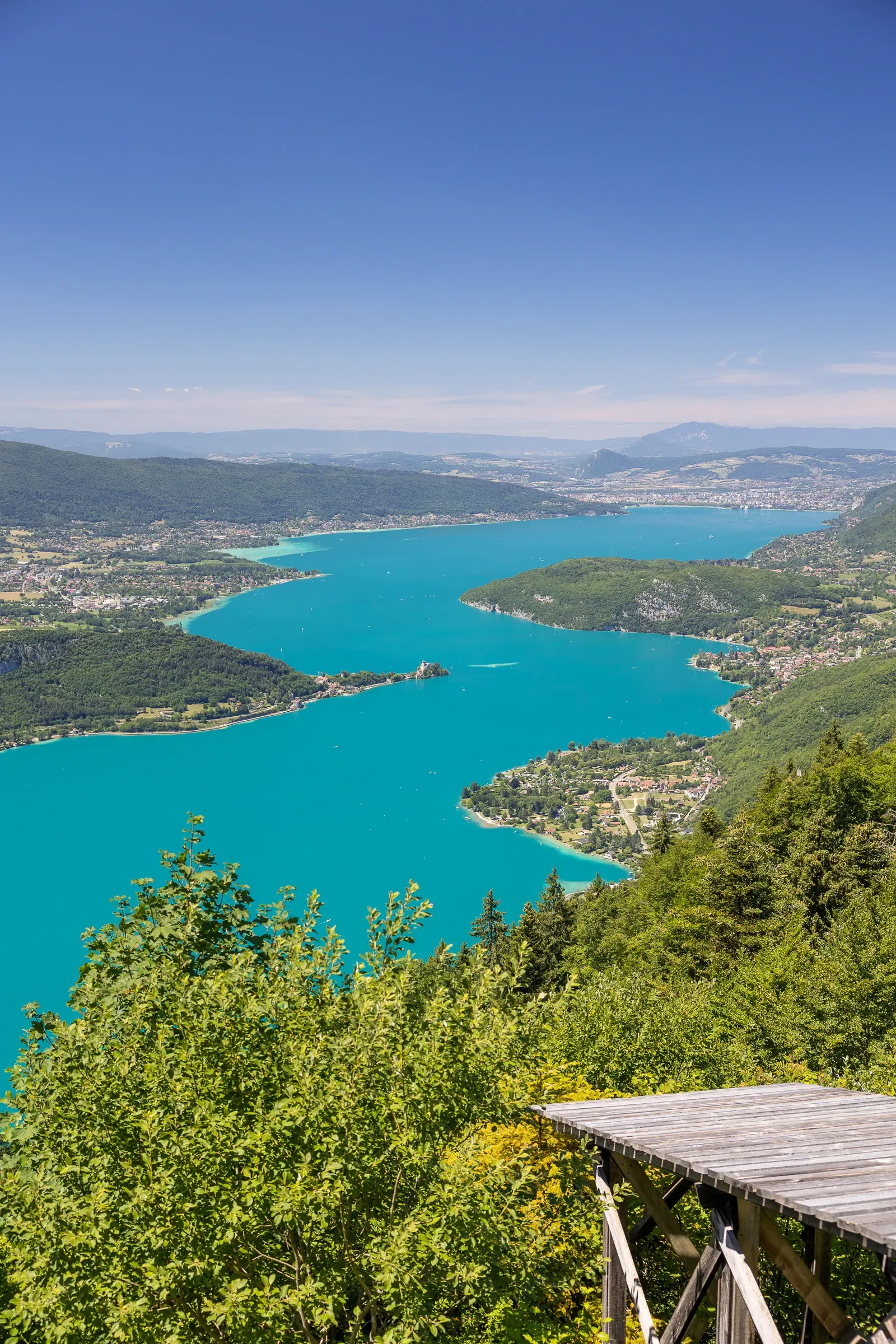 Aerial view of Lake Annecy from a hilltop viewpoint, turquoise water winding between forested mountains
