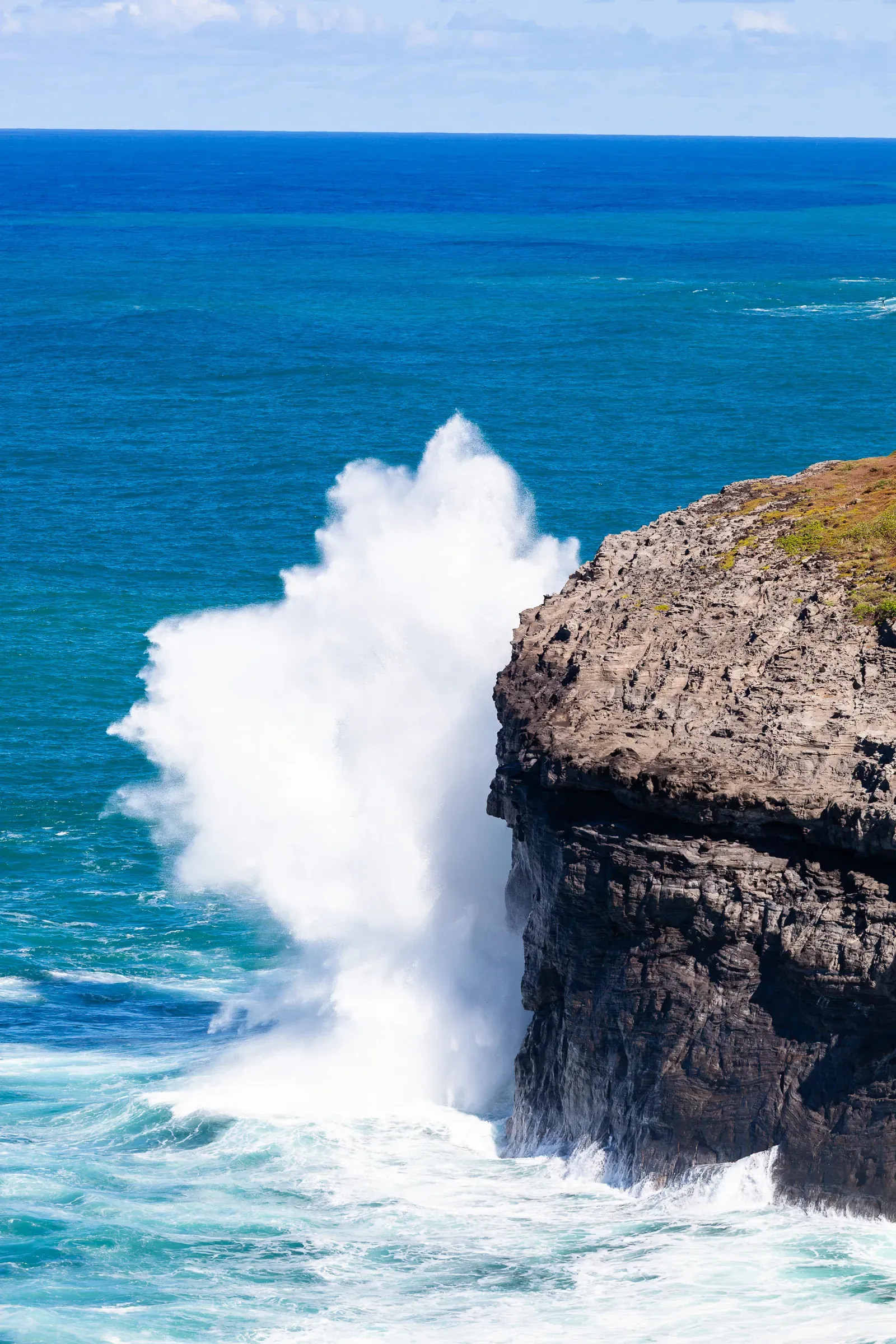 Wave exploding against a basalt cliff, Hawaii — white spray rising high against a turquoise ocean and clear sky