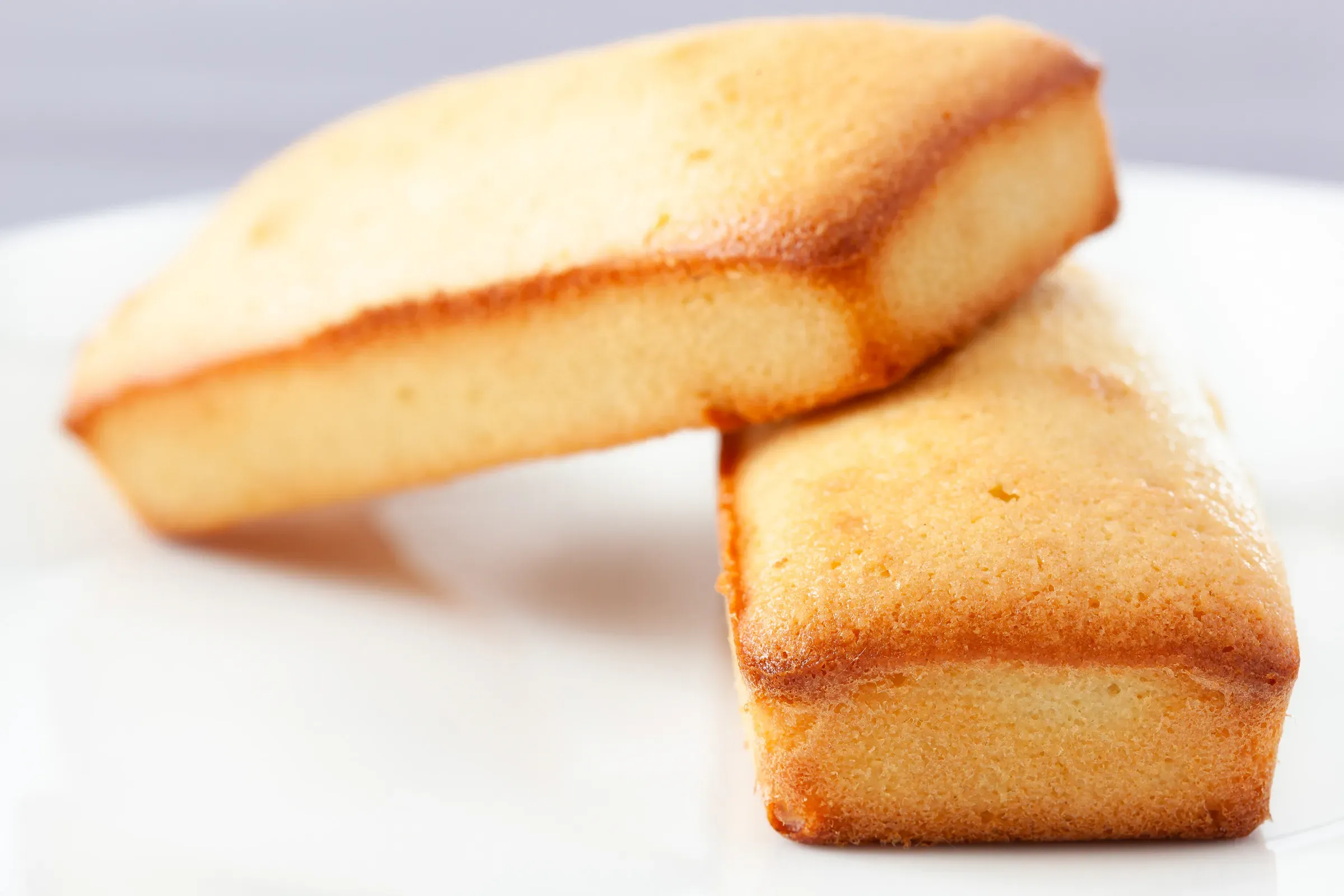 Two rectangular financiers resting against each other on a white surface, golden brown crust and pale almond crumb at the cut edge