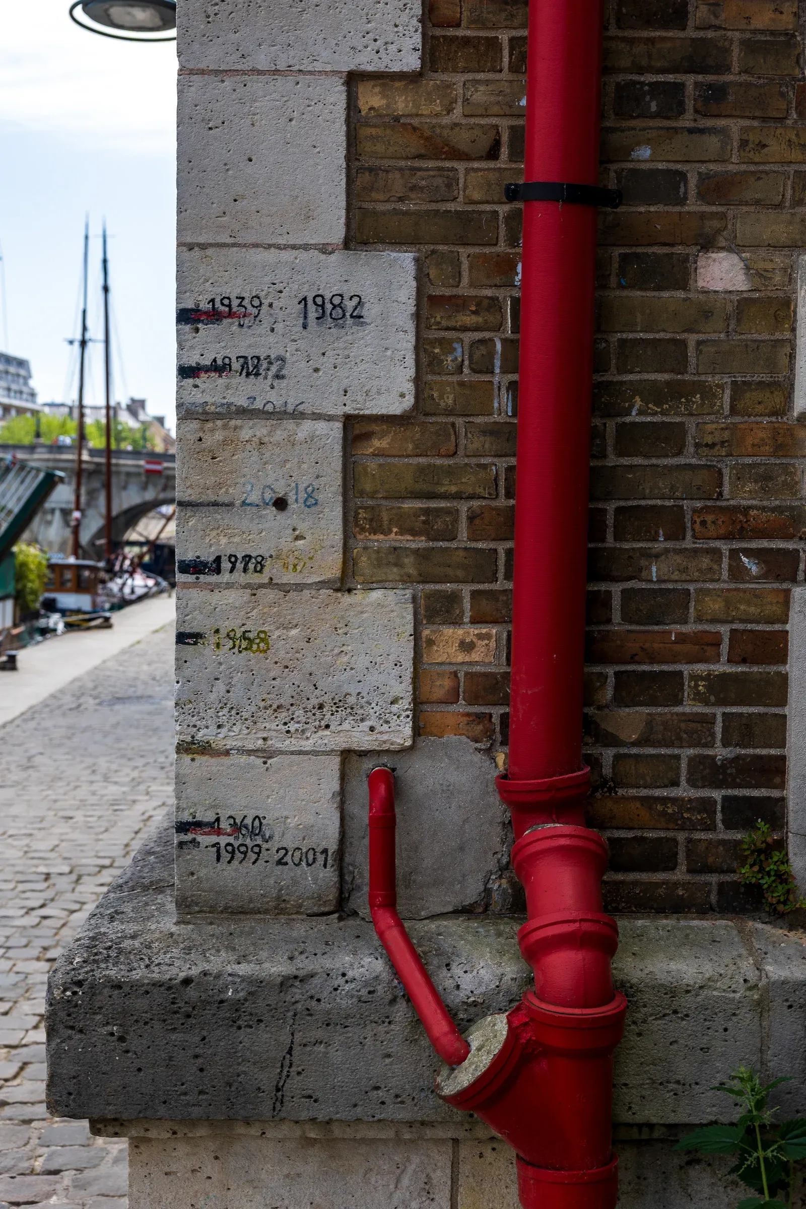 A red drainage pipe beside a stone wall marked with historical Seine flood-level years, quai of the Seine, Paris