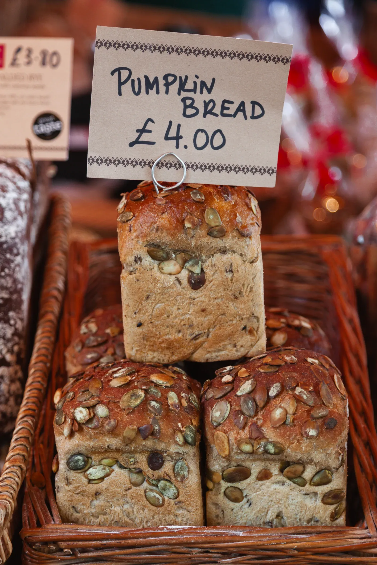 Pumpkin seed loaves stacked in a wicker basket with a handwritten sign reading Pumpkin Bread £4.00, Borough Market