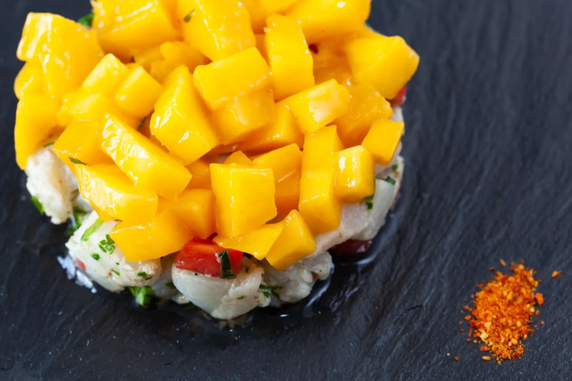 Crab and mango tartare on dark slate — diced mango piled over seafood, a small mound of paprika powder to one side