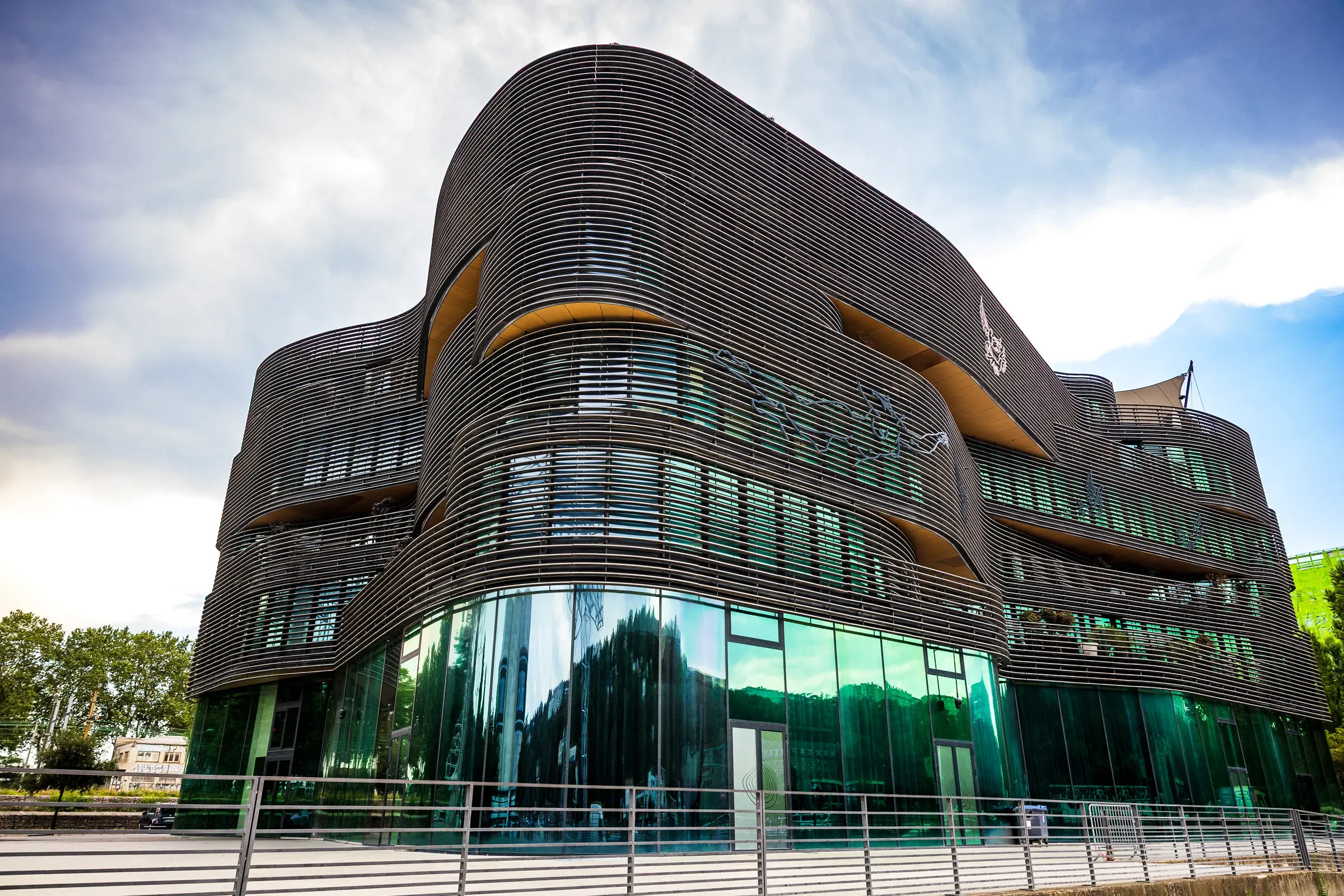 Modern curved building with dark horizontal metal louvers and a green glass base, Lyon