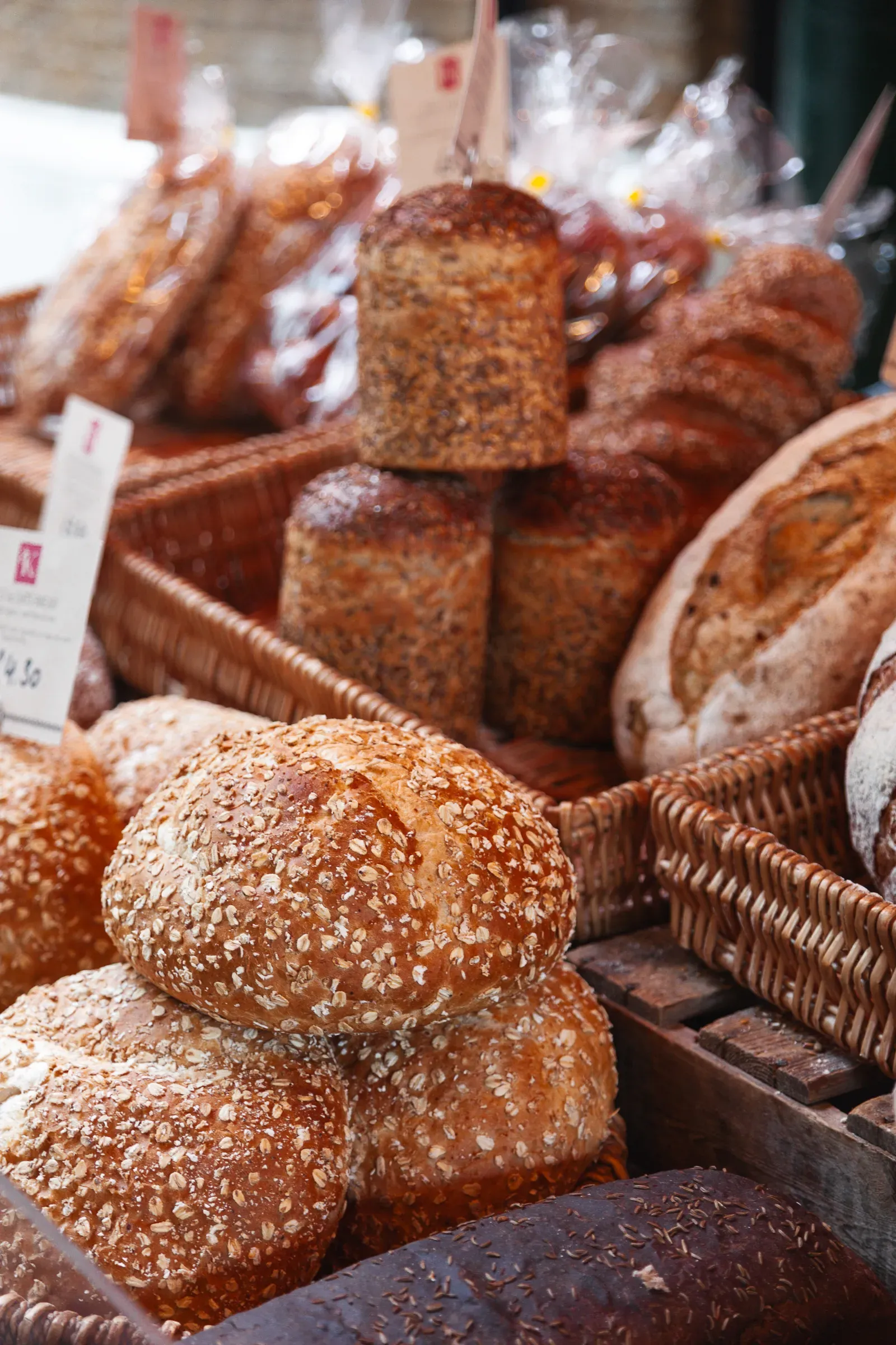 Artisan bread loaves — seeded rolls and round sourdoughs — piled in wicker baskets at a bakery stall