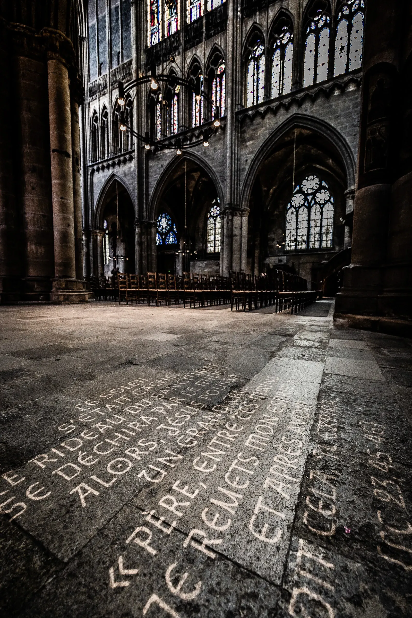 Wide nave of Metz Cathedral looking toward the entrance, scripture engraved on the floor in the foreground, light flooding through towering stained glass