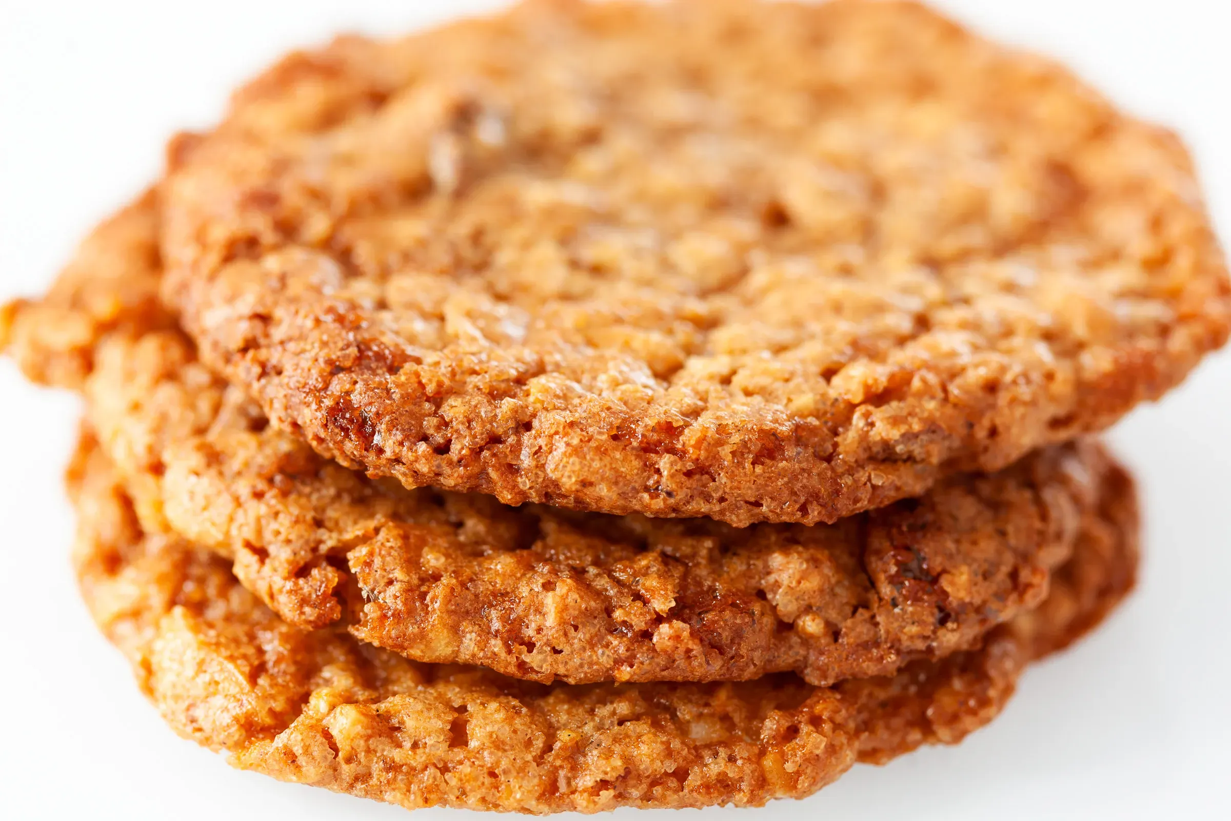 Stack of four golden oat cookies shot close from the side, rough craggy texture, white background