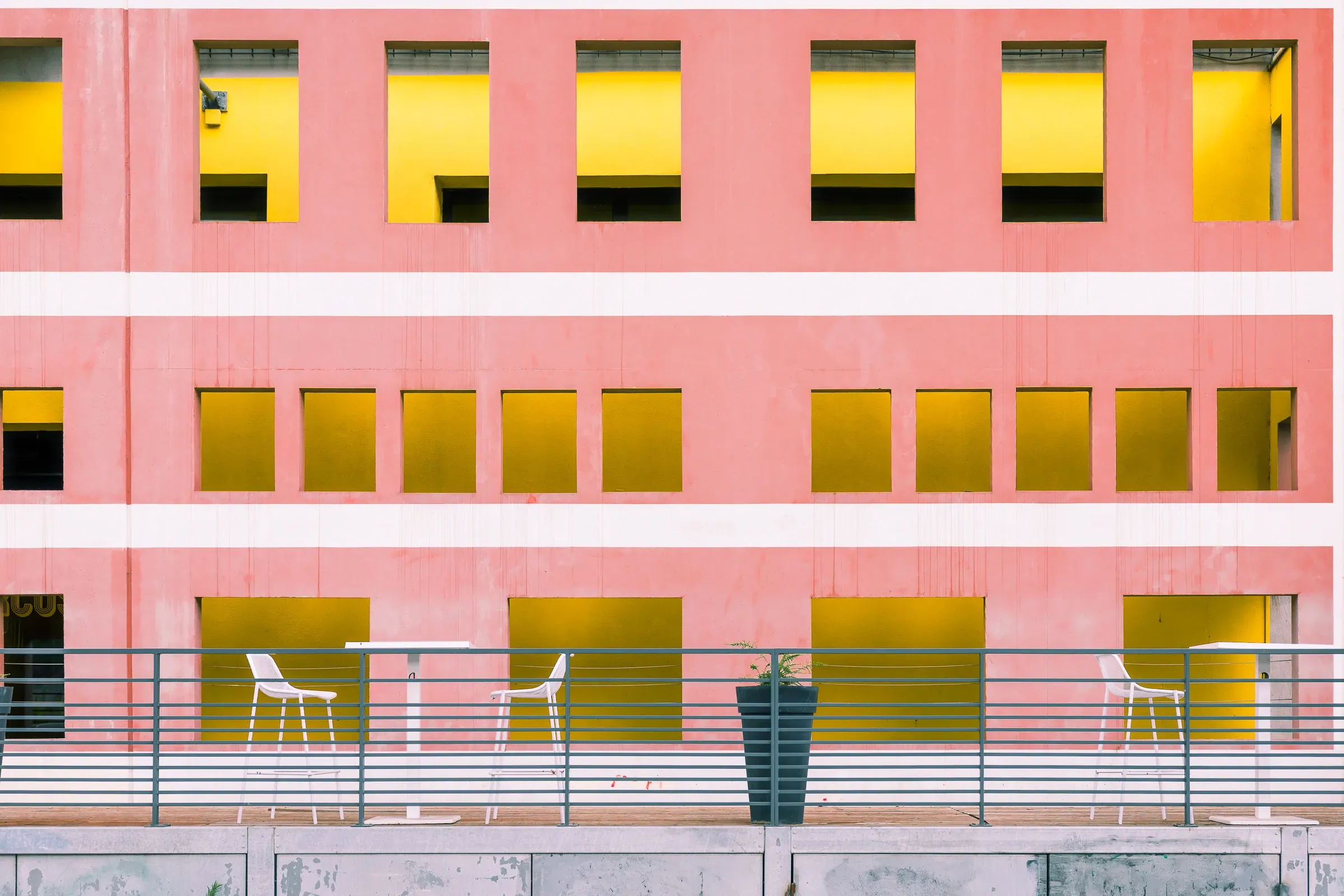 Pink and yellow building facade with a terrace, white chairs and a planter, Lyon