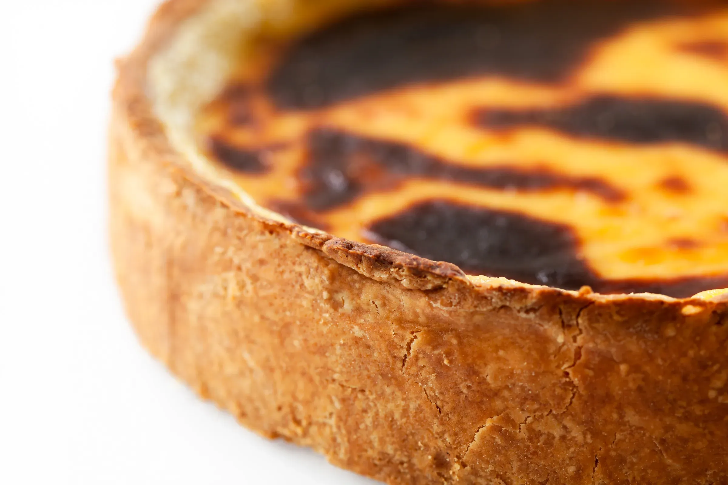 Burnt Basque cheesecake shot close at an angle — charred black and amber top, thick cracked crust, white background