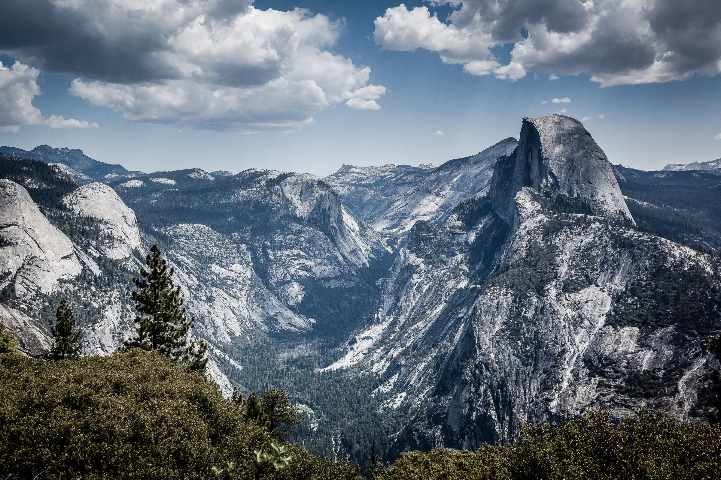 Half Dome and Yosemite Valley from Glacier Point — pine forest below, granite walls, moody cumulus clouds overhead