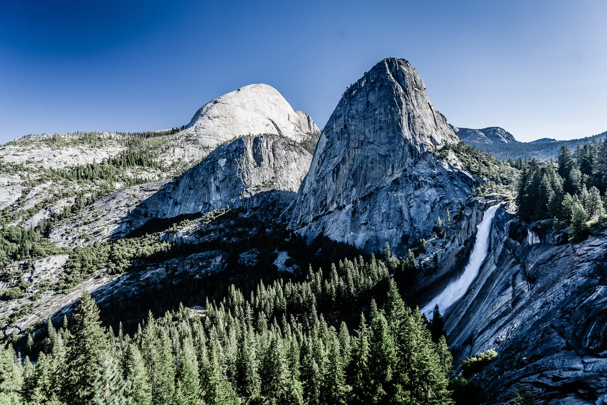 Half Dome and Liberty Cap from the John Muir Trail, Yosemite — Nevada Fall visible in the right cliff face, deep blue sky