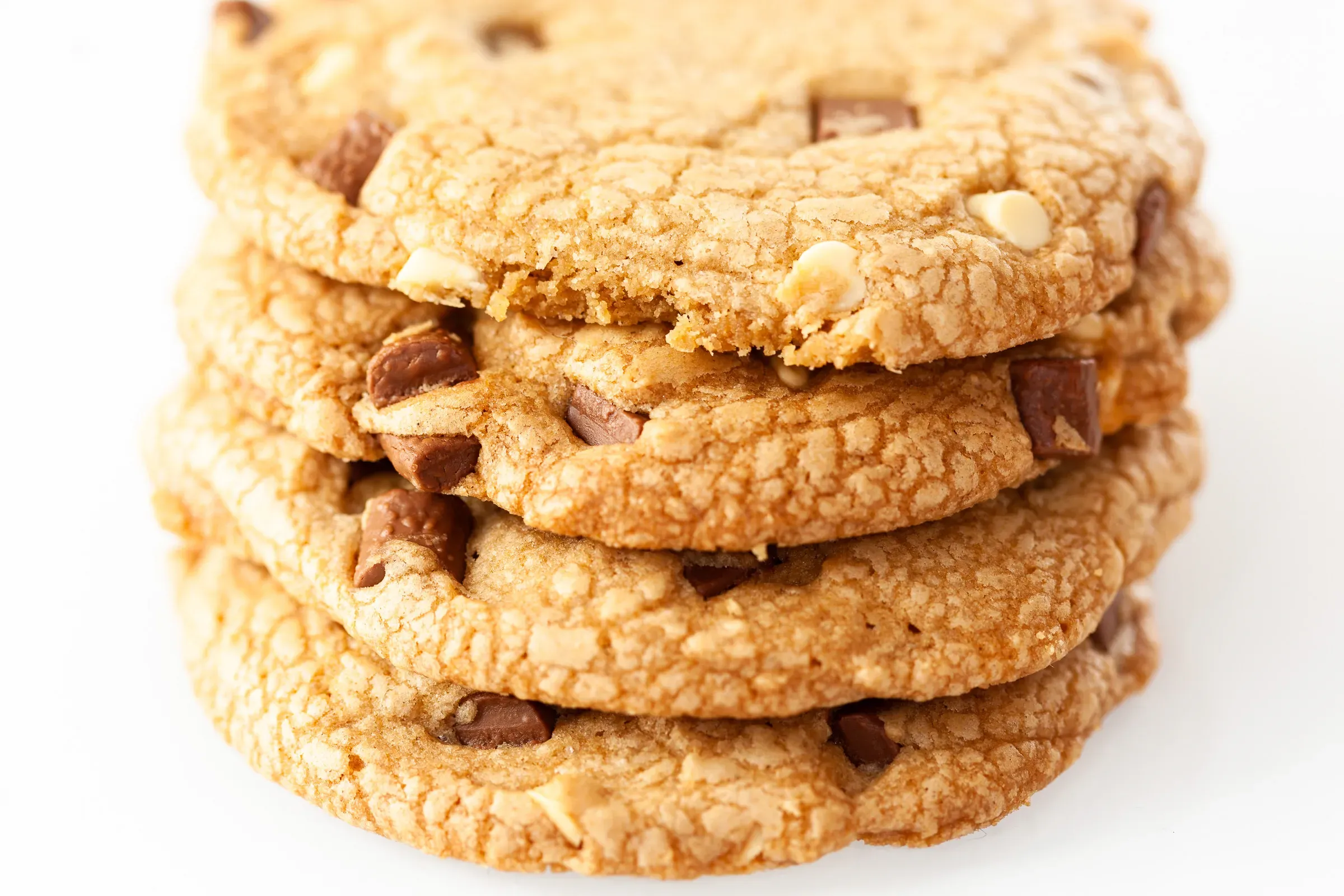 Stack of five chocolate chip cookies shot close from the side, top cookie slightly broken, white background