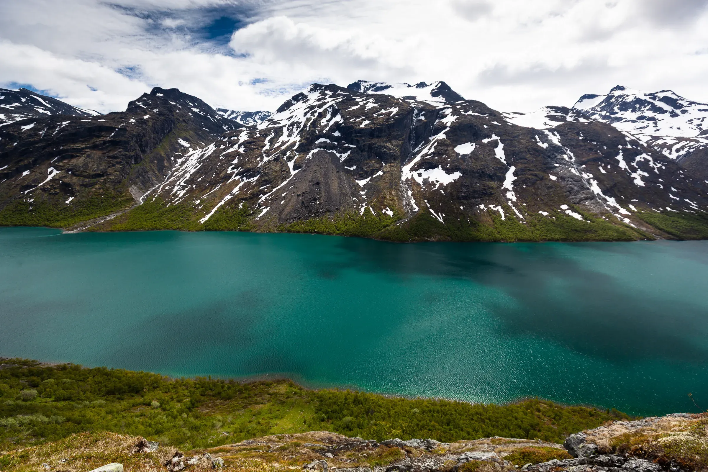 Lake Gjende from above, Jotunheimen — still turquoise water reflecting snow-covered peaks, green tundra in the foreground