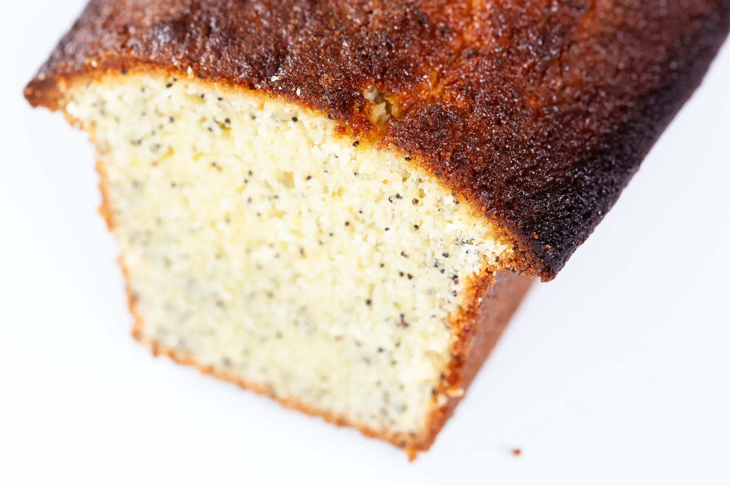 Lemon and poppy seed loaf, one end sliced off to reveal the speckled pale crumb, golden crust, white surface